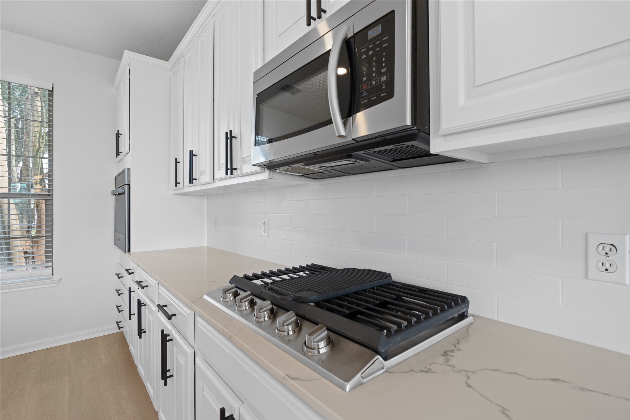 Kitchen Cooktop Close-up highlights the gas cooktop, stainless steel microwave, white subway-style backsplash, stone-look countertop, and abundant surrounding cabinetry. Kitchen Cooktop Close-up highlights the gas cooktop, stainless steel microwave, white subway-style backsplash, stone-look countertop, and abundant surrounding cabinetry.
