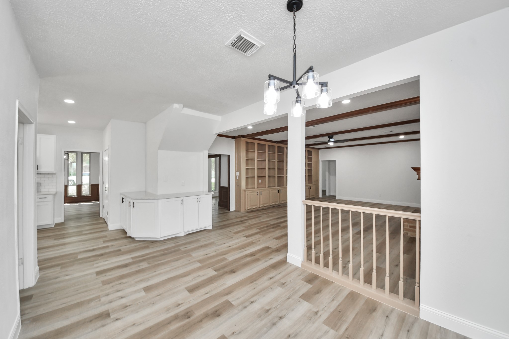 Spacious open-concept living area featuring elegant wood flooring, built-in shelving, and modern light fixtures, seamlessly connecting to the kitchen and dining spaces.