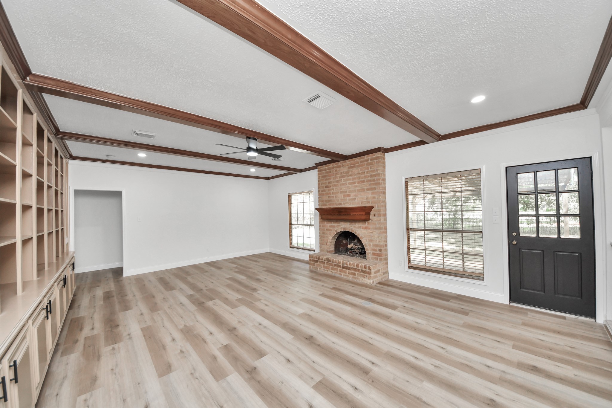Spacious living room featuring elegant wood-beamed ceilings, a cozy brick fireplace, built-in shelving, and abundant natural light.