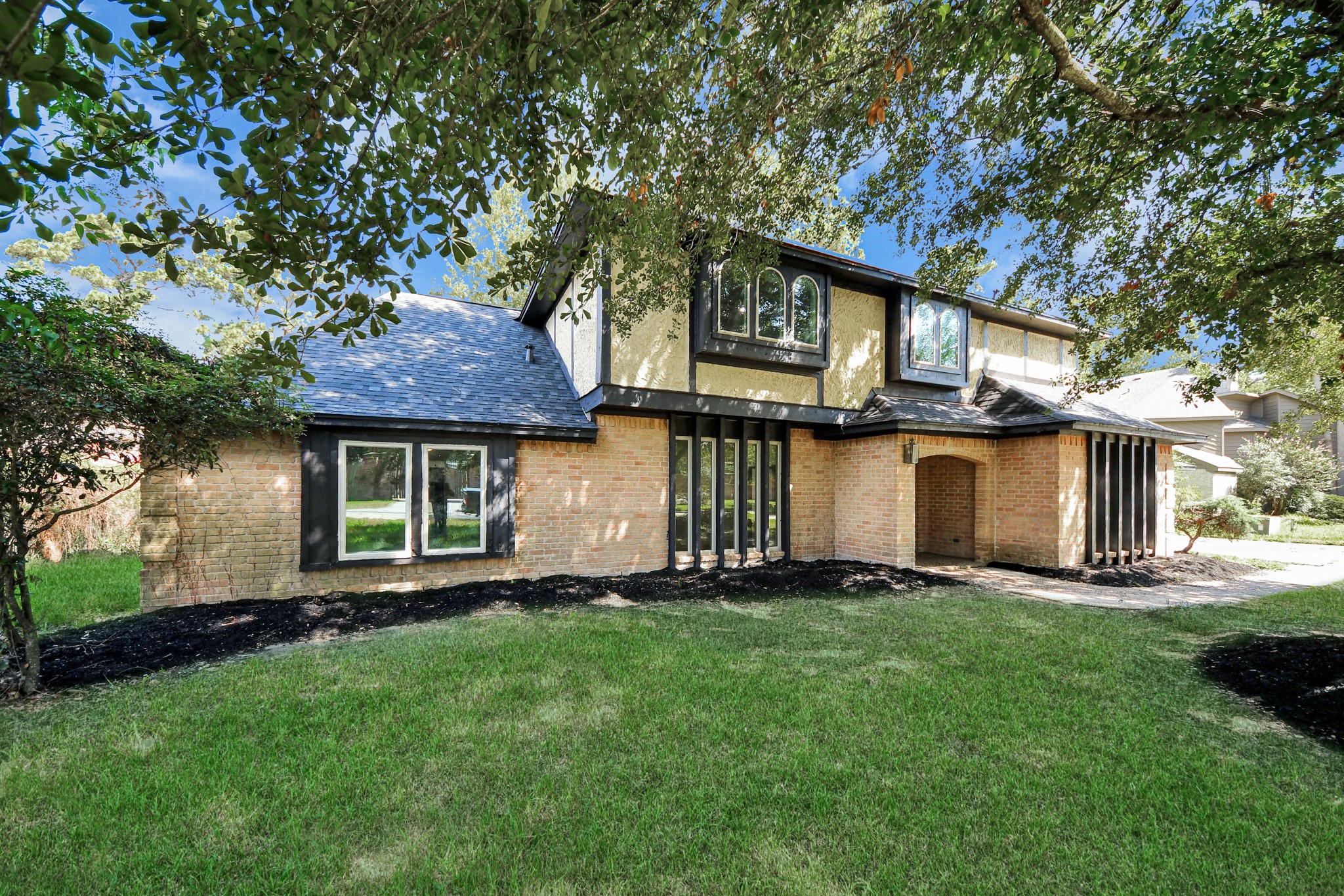 Charming two-story home with a mix of brick and wood accents, nestled among mature trees.