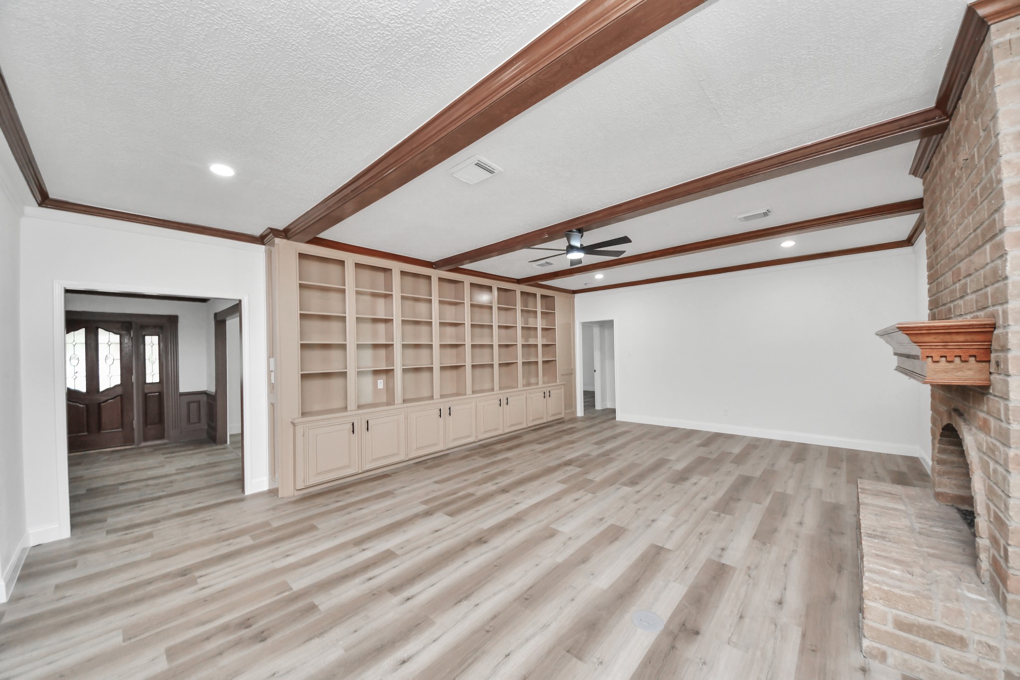 Spacious living room with elegant built-in shelving, a cozy brick fireplace, and rich wooden ceiling beams, perfect for relaxation and entertaining.