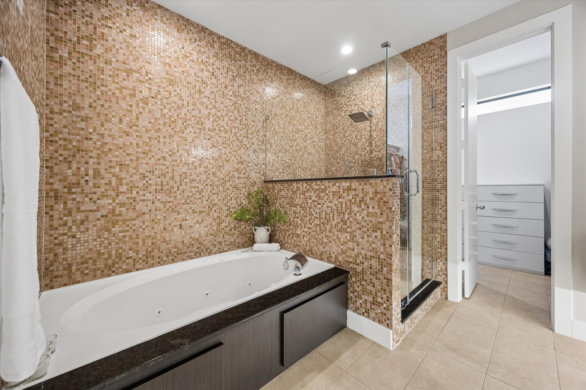 The primary bath brings a spa-like feel to everyday routines with a jetted soaking tub, glass-enclosed shower, warm mosaic tile, and sleek modern finishes. Direct access to the custom walk-in closet keeps mornings easy, while the polished design makes the whole space feel calm and relaxing.