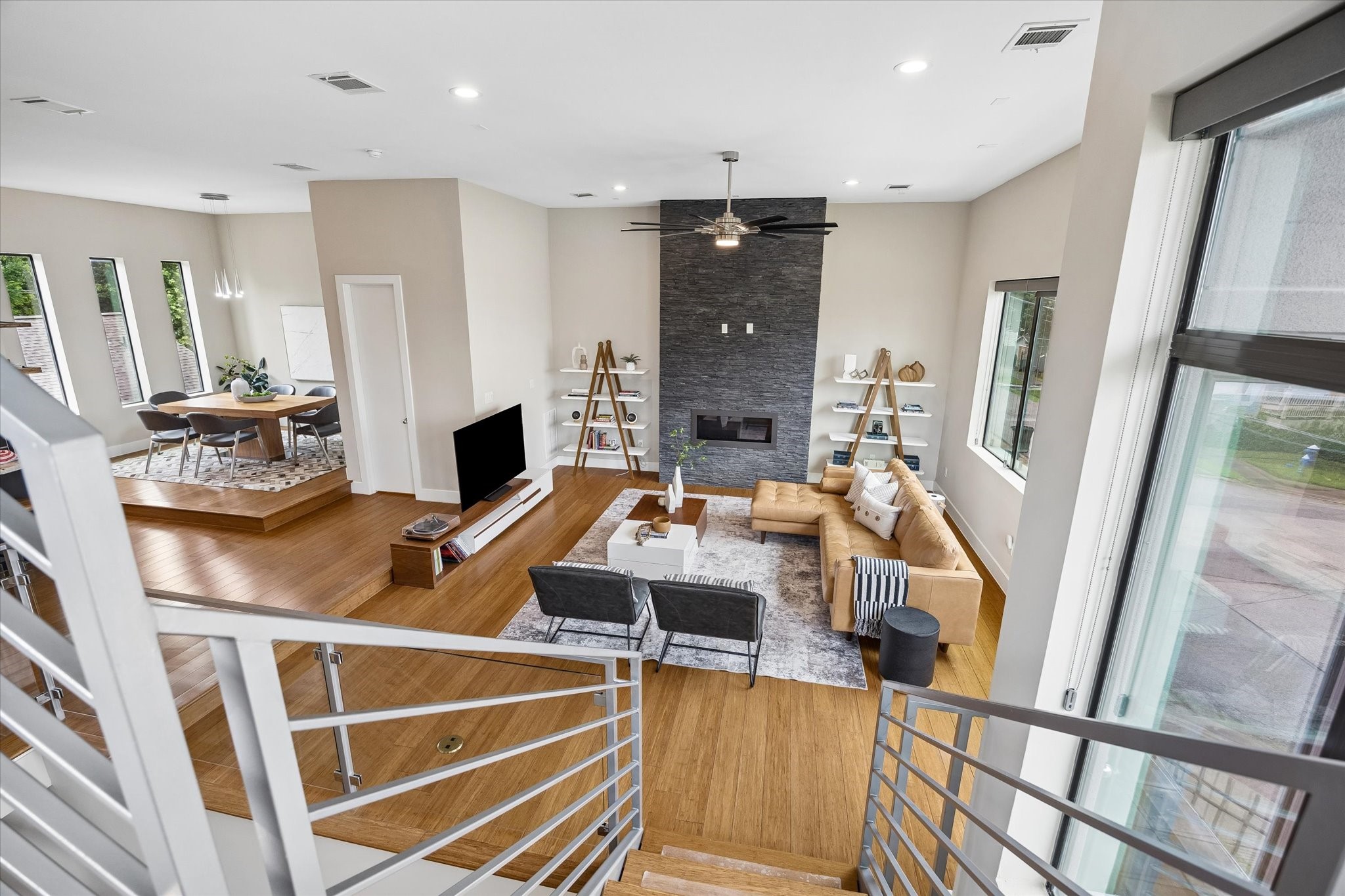 From the staircase landing, youll get a great sense of the homes open, airy design, with the living, dining, and kitchen spaces all connected below. Warm wood flooring, tall windows, modern railings, and the sleek fireplace come together to make this main living level feel bright, stylish, and easy to love.