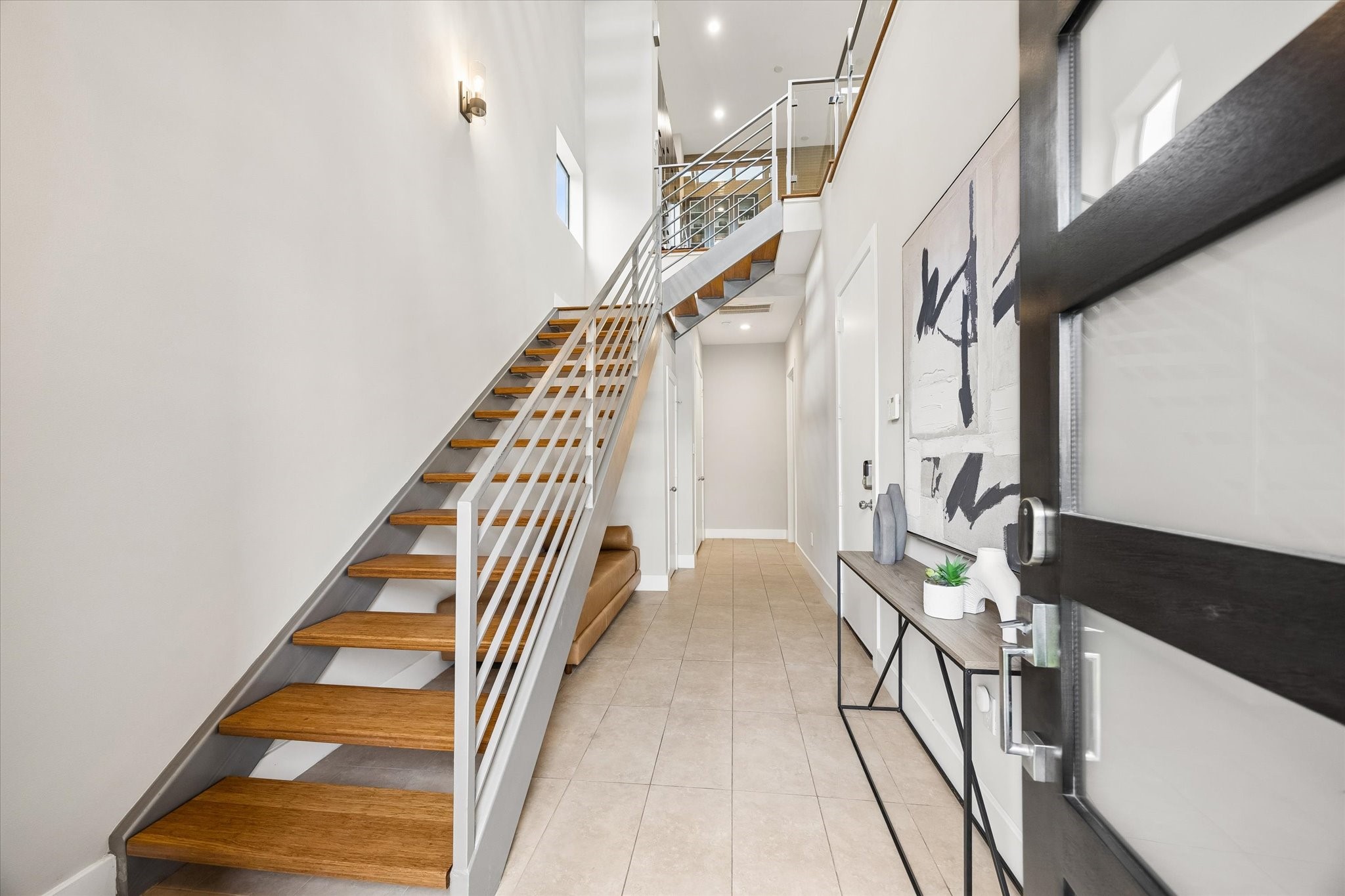 Sleek finishes begin right at the front door, where the bright first-floor entry makes a crisp, modern first impression with a soaring ceiling, clean tile flooring, and a statement staircase that carries the style upward.