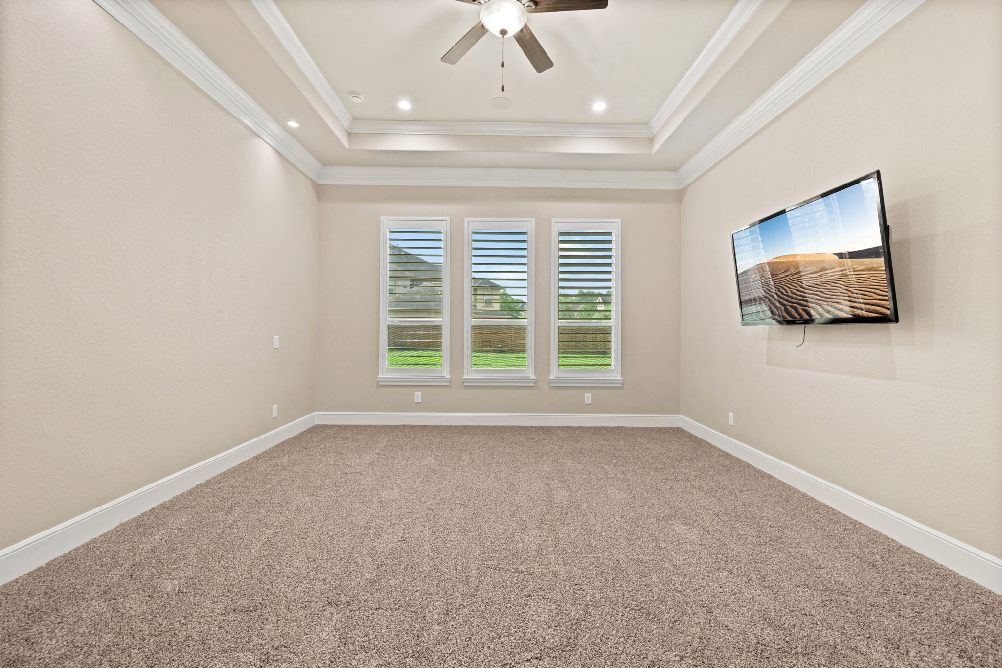 Primary bedroom showcasing a tray ceiling and has custom lighting and a ceiling fan.
