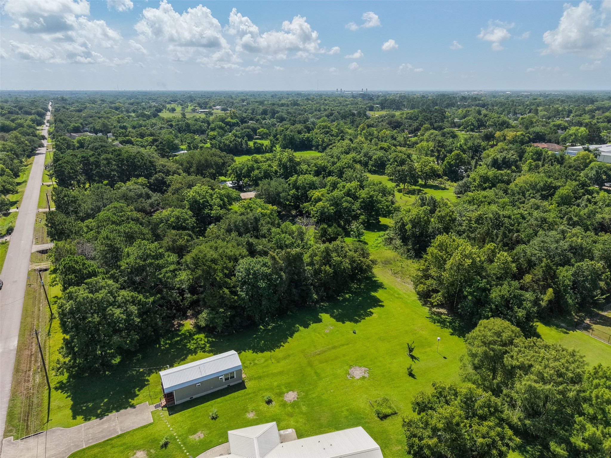 Looking along 28th Street illustrates the property's convenient position within an established semi-rural area of Santa Fe. The straight paved roadway provides direct access to FM 646, while the surrounding landscape remains dominated by mature trees and generously sized properties. This combination of accessibility, acreage and natural character makes the site especially compelling for buyers seeking space without feeling isolated.