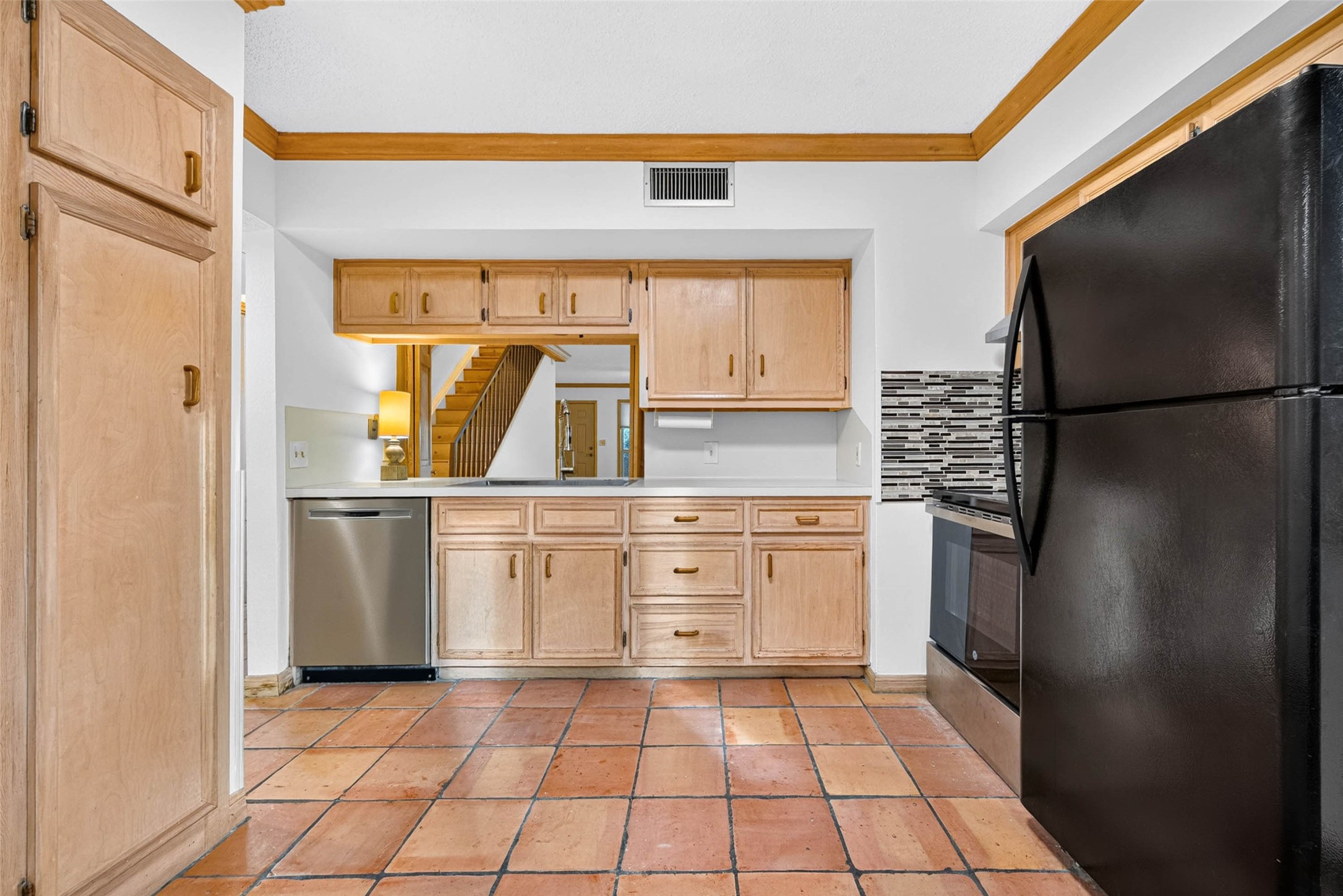 Charming kitchen featuring natural wood cabinets, a sleek black refrigerator, and modern appliances, complemented by a stylish tile backsplash and warm flooring.