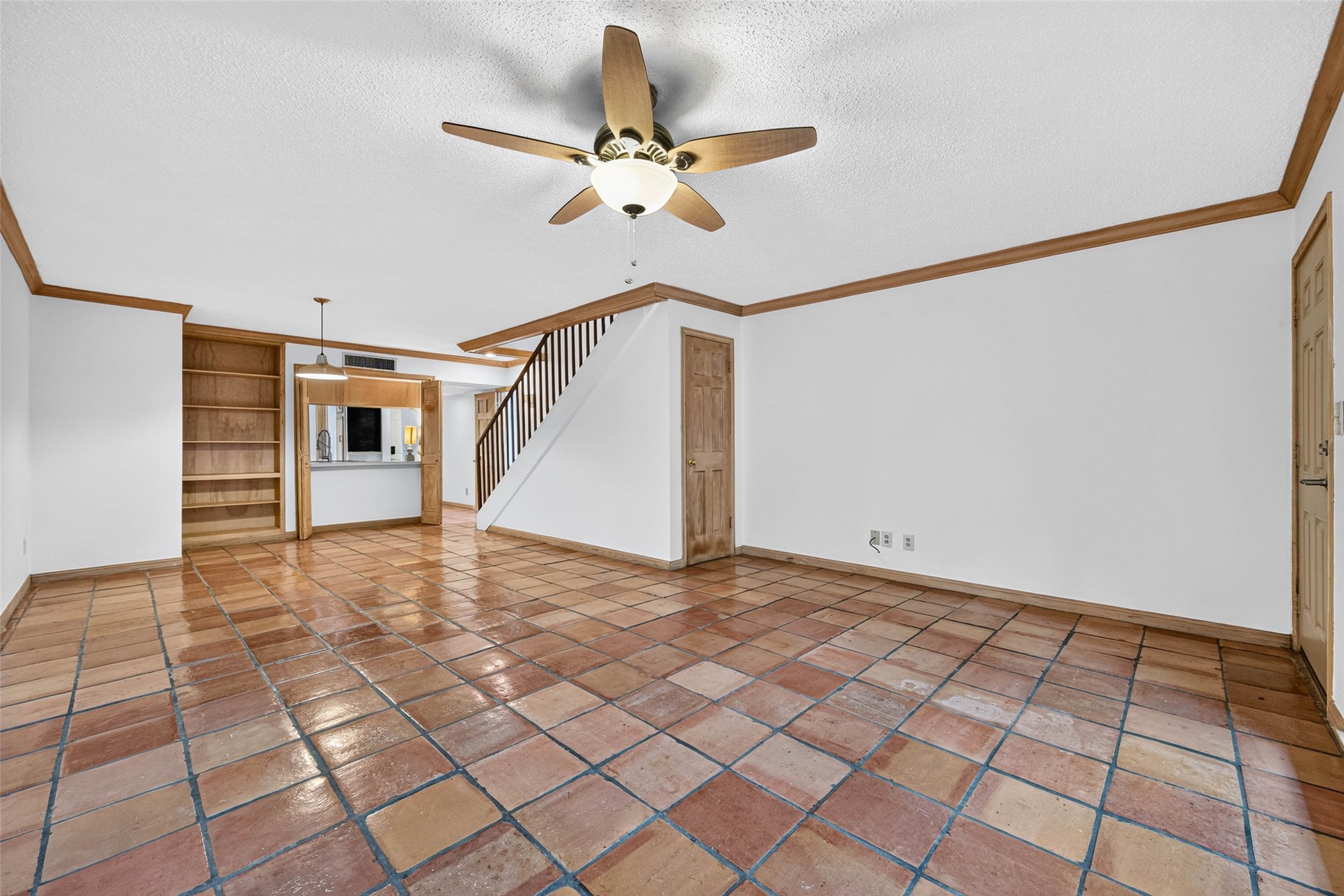 Spacious living area elegant wood trim, built-in shelving, and a ceiling fan, leading to an open kitchen and staircase.