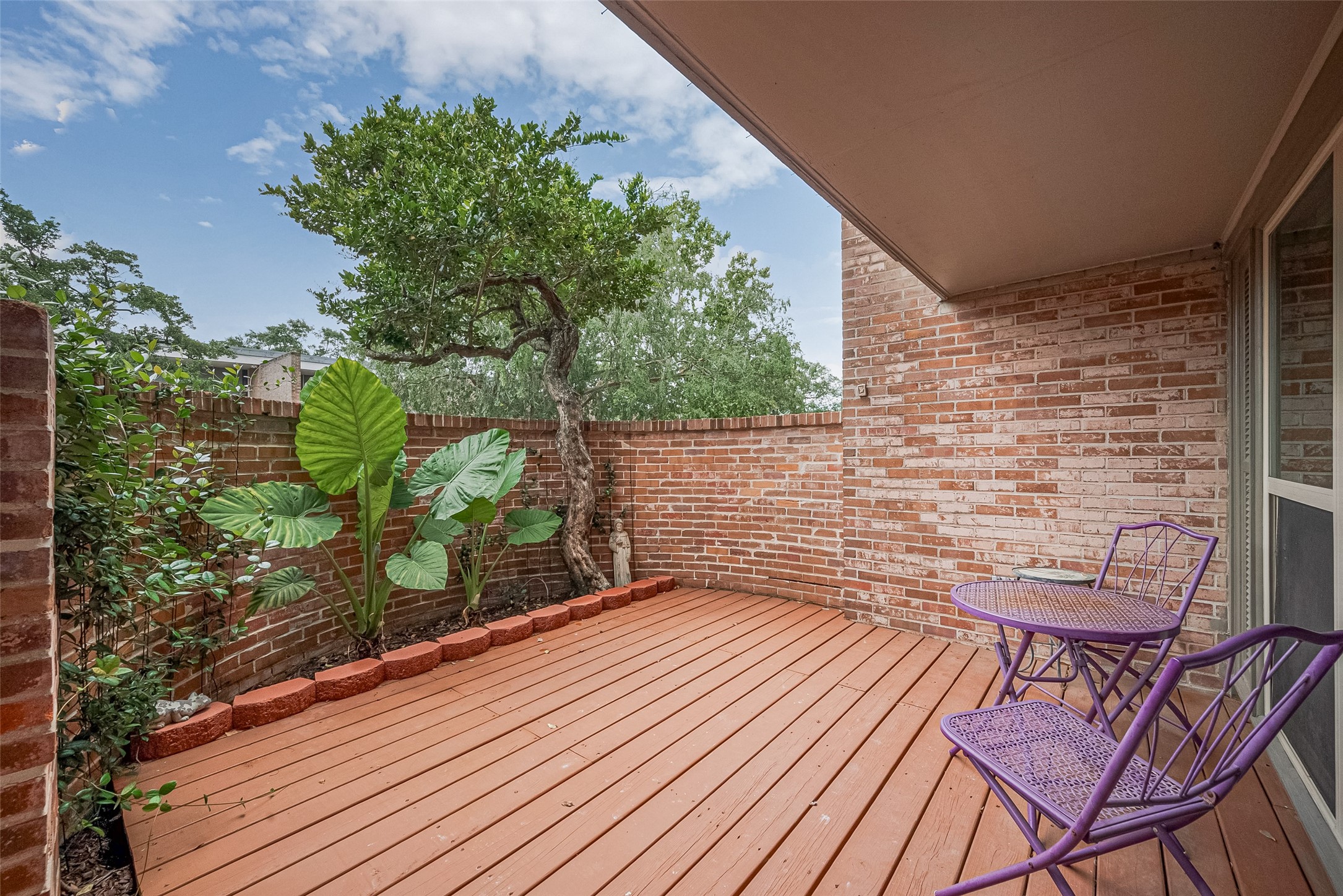 Charming private patio with warm brick walls, lush greenery, and a cozy seating area perfect for relaxation and outdoor dining.