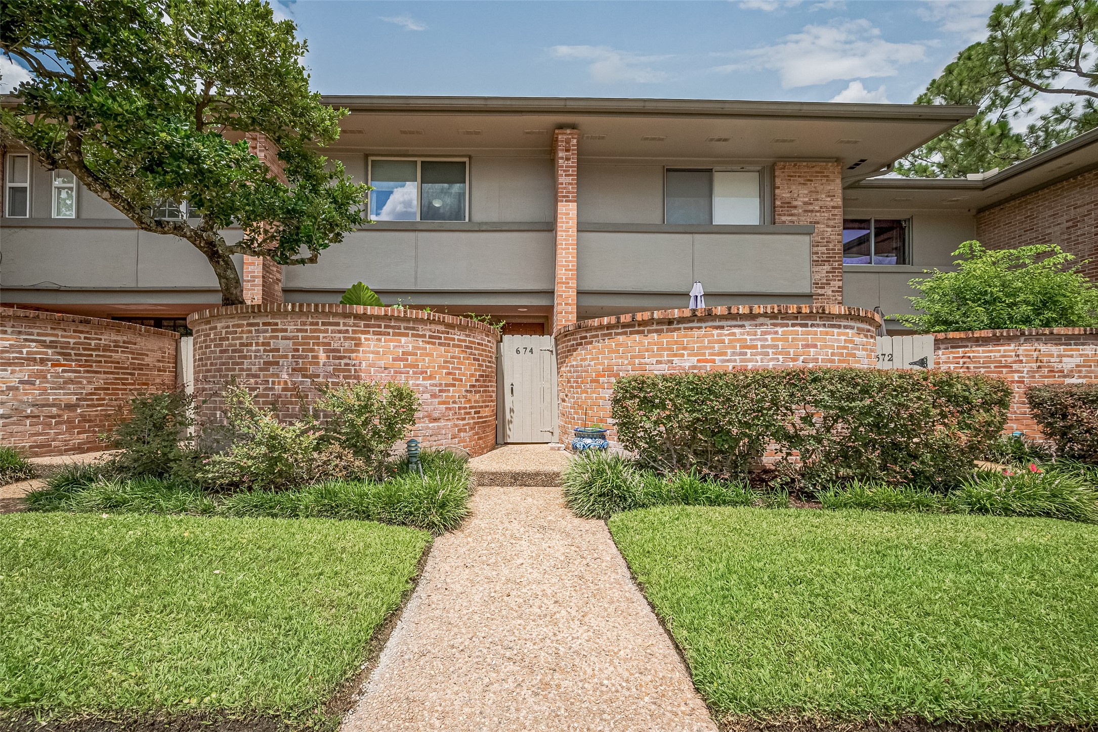 Charming two-story townhouse with a classic brick exterior and private gated entrance, surrounded by lush landscaping and mature trees. Charming two-story townhouse with a classic brick exterior and private gated entrance, surrounded by lush landscaping and mature trees.