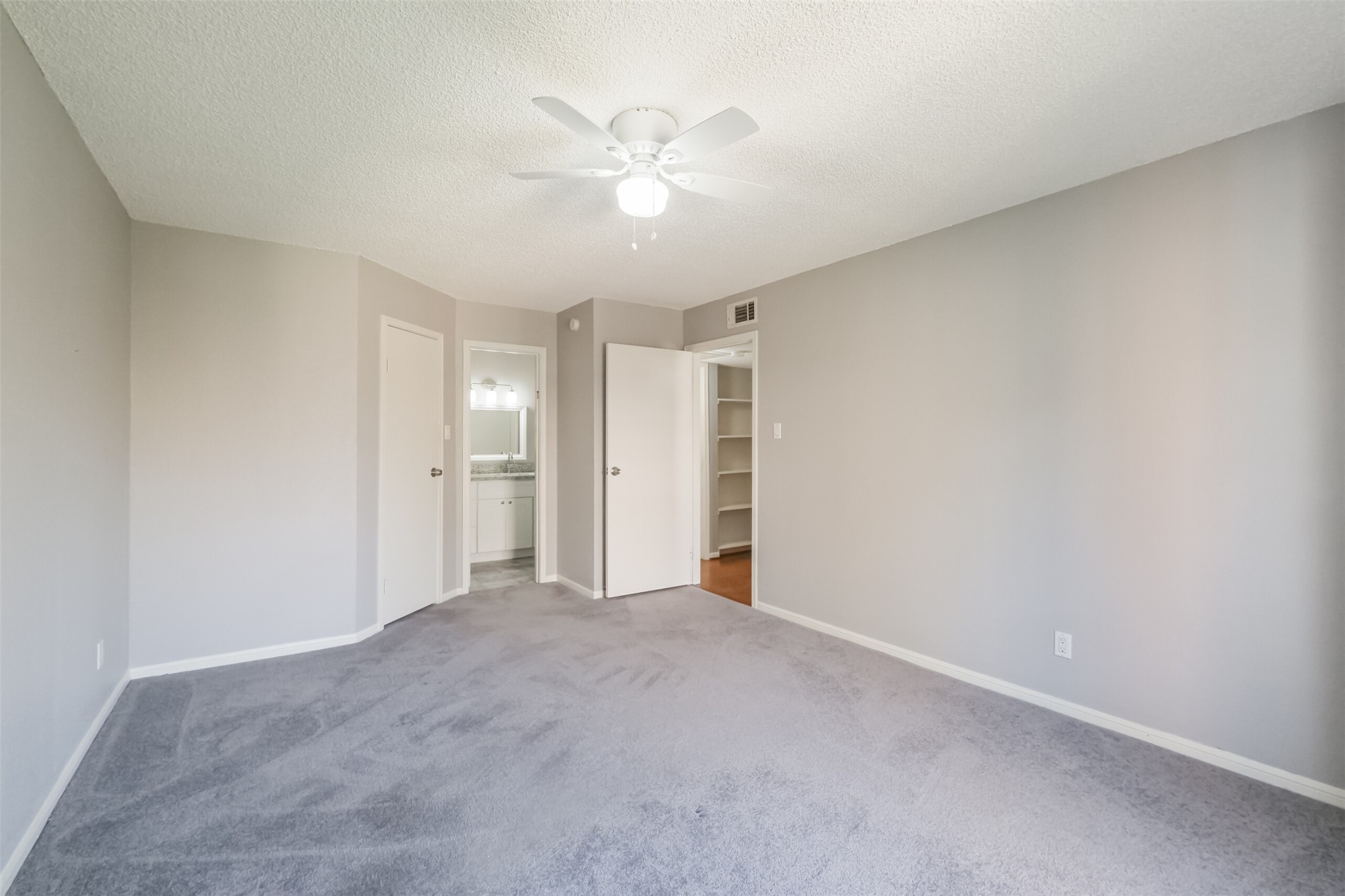 Spacious primary bedroom with carpeted floors and a ceiling fan!