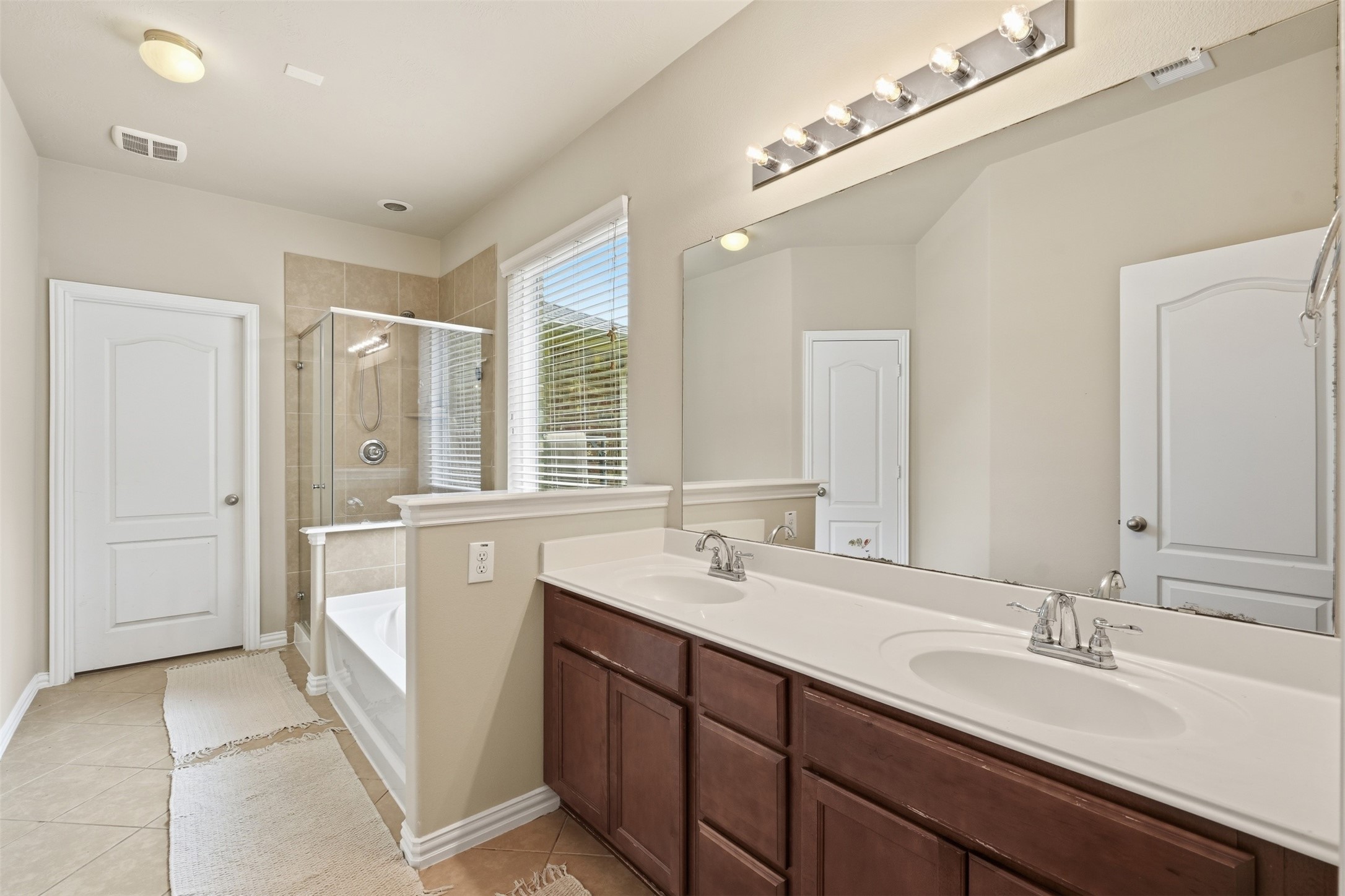A primary bath with spa-day energy: double-sink vanity, oversized mirror, garden soaking tub and a separate glass-enclosed shower.