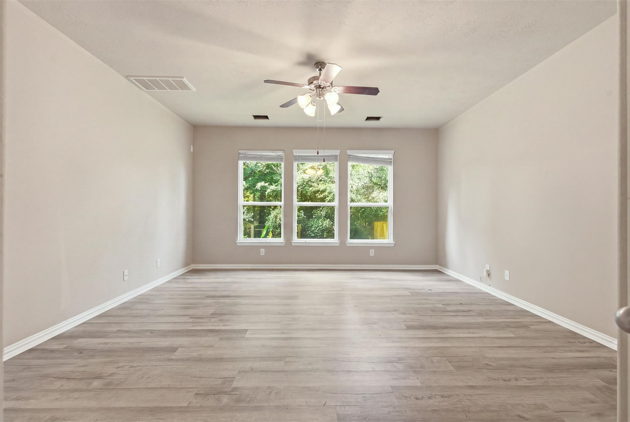 Welcome to the primary retreat, on the main floor and away from the upstairs bedrooms. About 17x16, with a triple window framing the trees, a ceiling fan and wood-look plank floors.