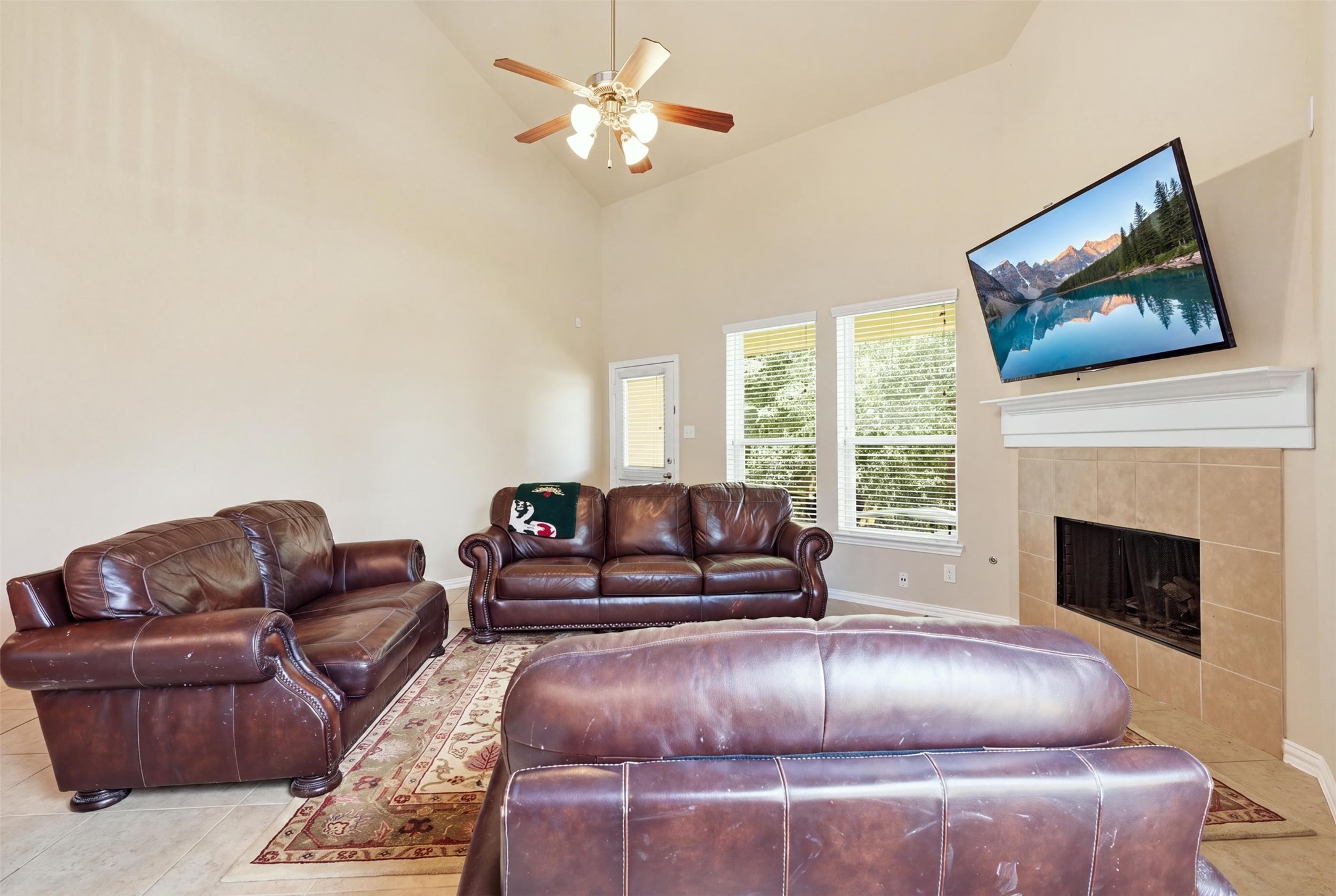 Big-sky living room: soaring ceilings, a gas-log fireplace with tile surround and mantel, and a wall of windows framing the green view out back. The door to the covered patio is right here. Big-sky living room: soaring ceilings, a gas-log fireplace with tile surround and mantel, and a wall of windows framing the green view out back. The door to the covered patio is right here.