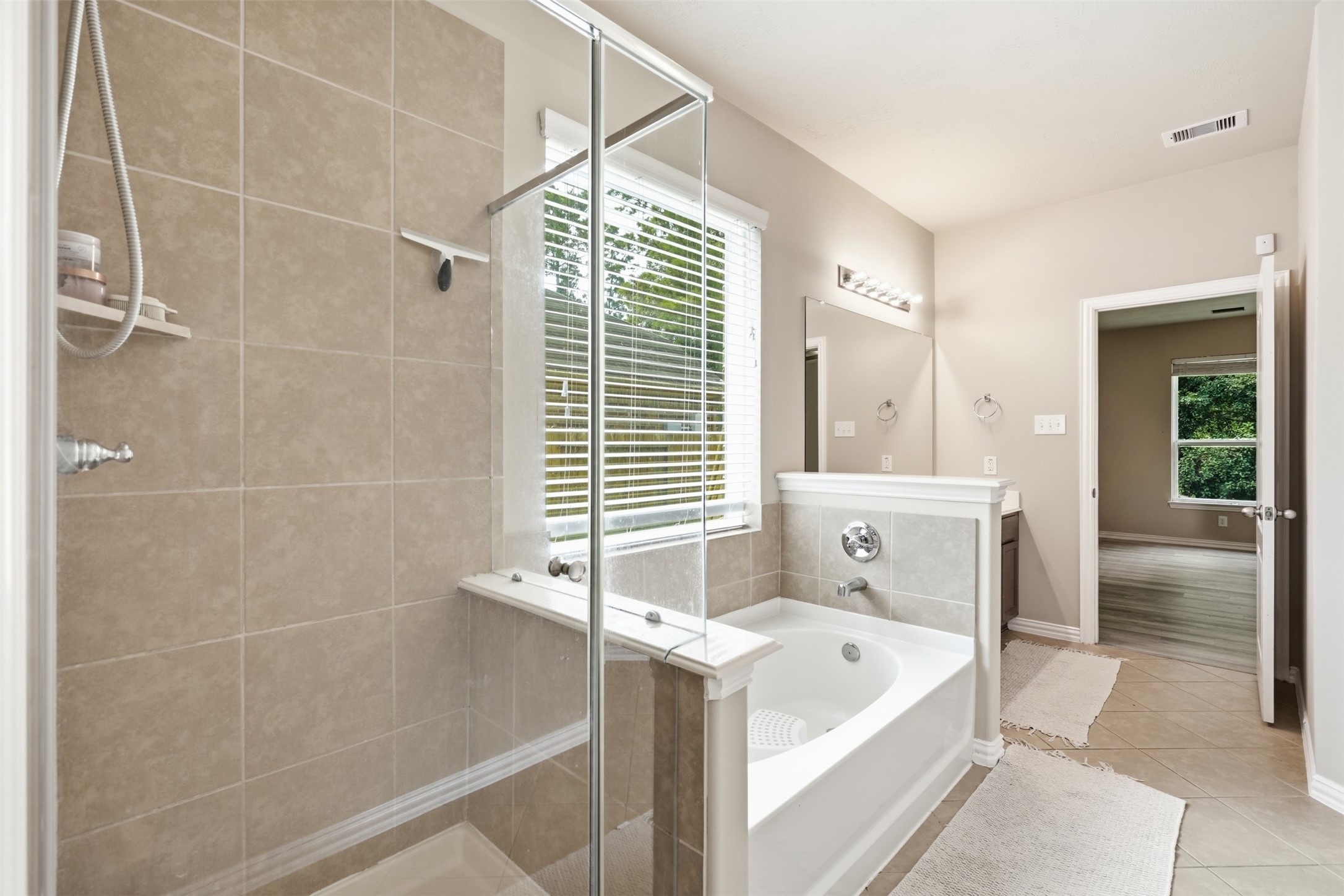 Soak or rinse, your call. The garden tub and walk-in glass shower sit side by side under a window, with the bedroom just steps away.