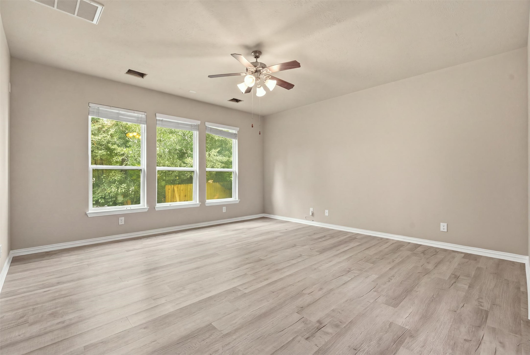 One more angle of the roughly 17x16 primary bedroom: bright, neutral and move-in ready, with a ceiling fan and three windows facing the backyard.