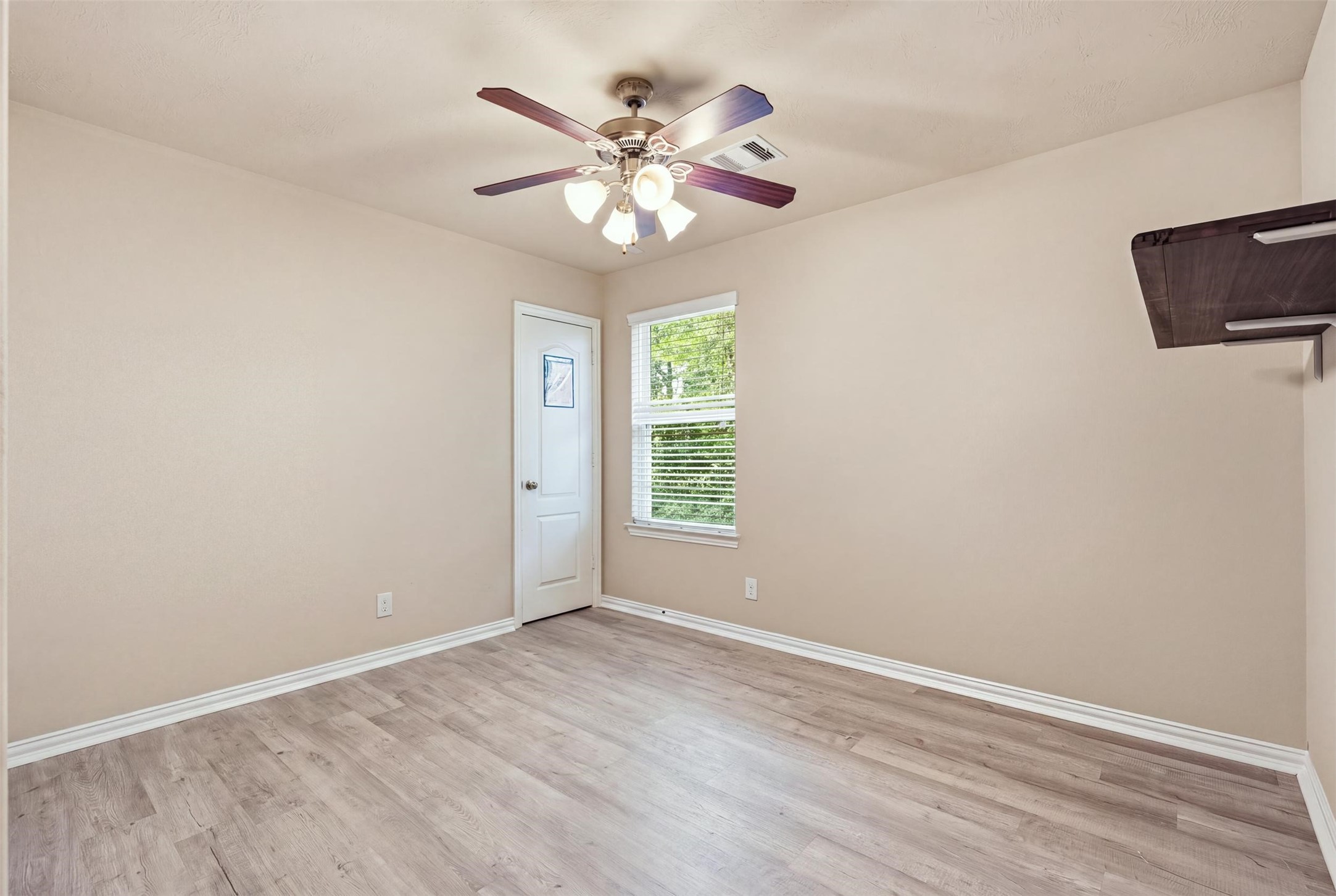 A blank-canvas bedroom with treetop views, a ceiling fan and wood-look plank floors. Guest room, hobby room or office: make it yours.