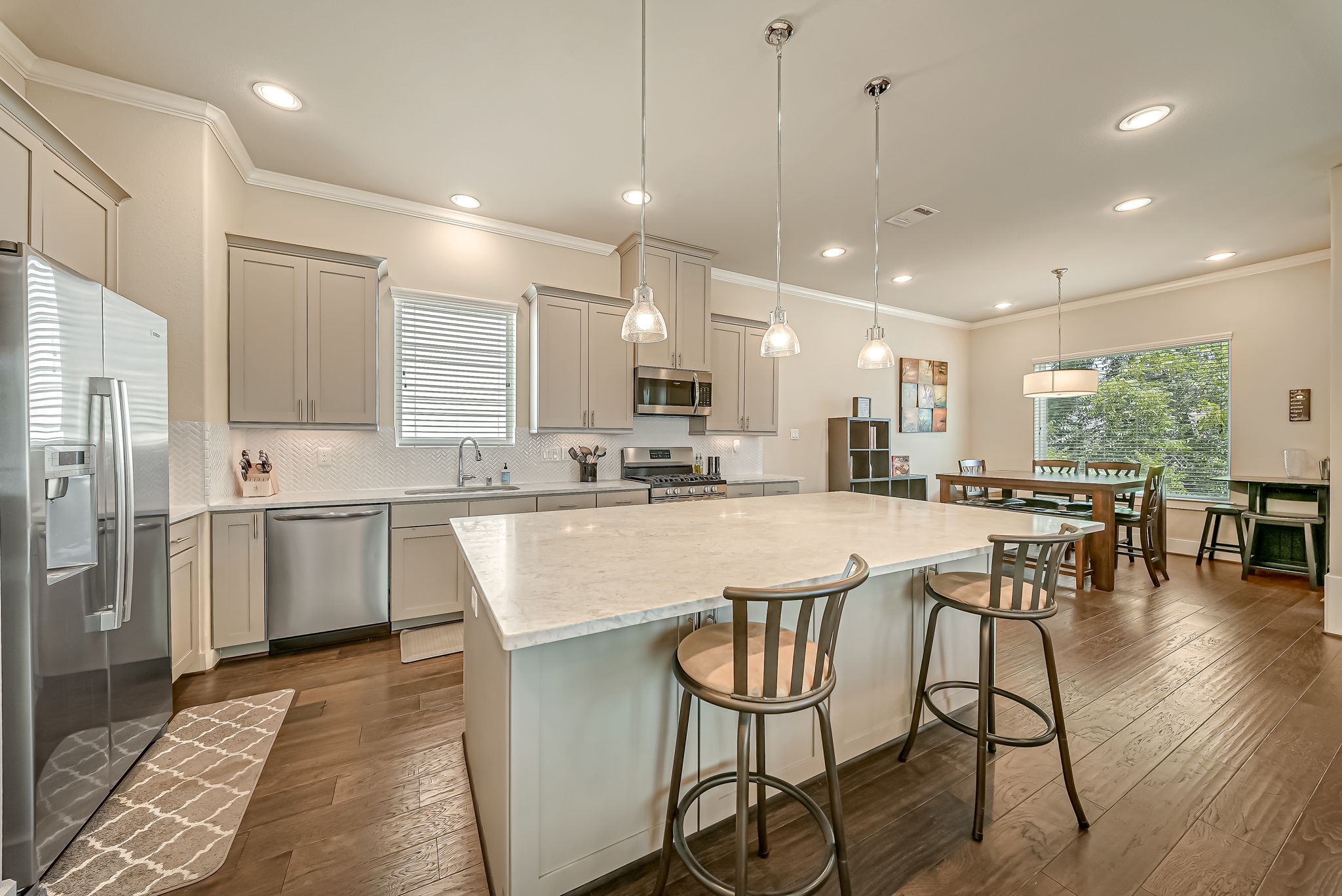 Chef-inspired kitchen showcasing an oversized marble island, stainless steel appliances, soft-close cabinetry, wine chiller, and stylish herringbone backsplash.