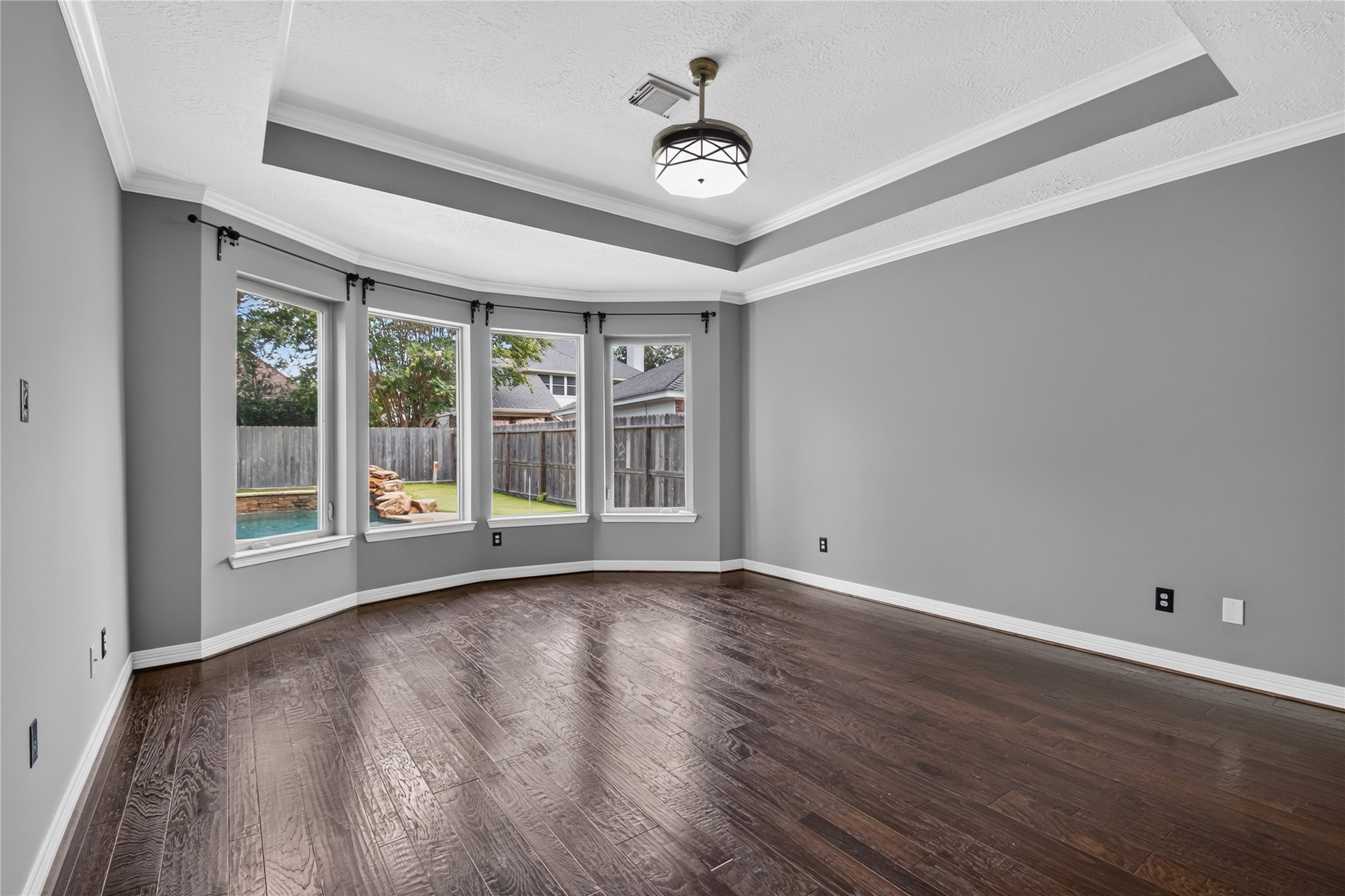 Spacious first-floor primary bedroom with REAL WOOD FLOORS, tray ceiling and a wall of windows overlooking the backyard.