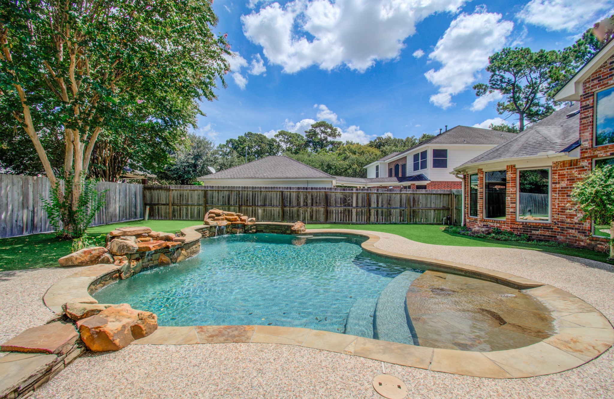 PRIVATE BEACH-ENTRY PEBBLETEC POOL with rock waterfalls creates a backyard retreat made for Texas summers.