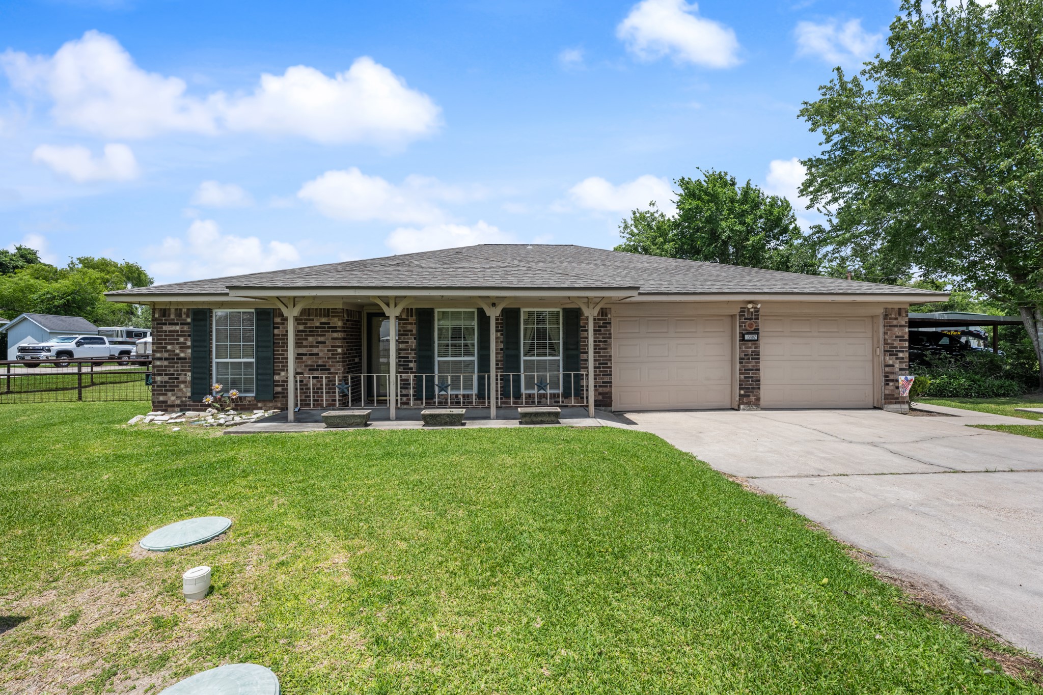 Charming single-story brick home featuring a welcoming covered front porch, mature shade trees, and an expansive front lawn. The attached two-car garage and additional covered parking provide added convenience and functionality.