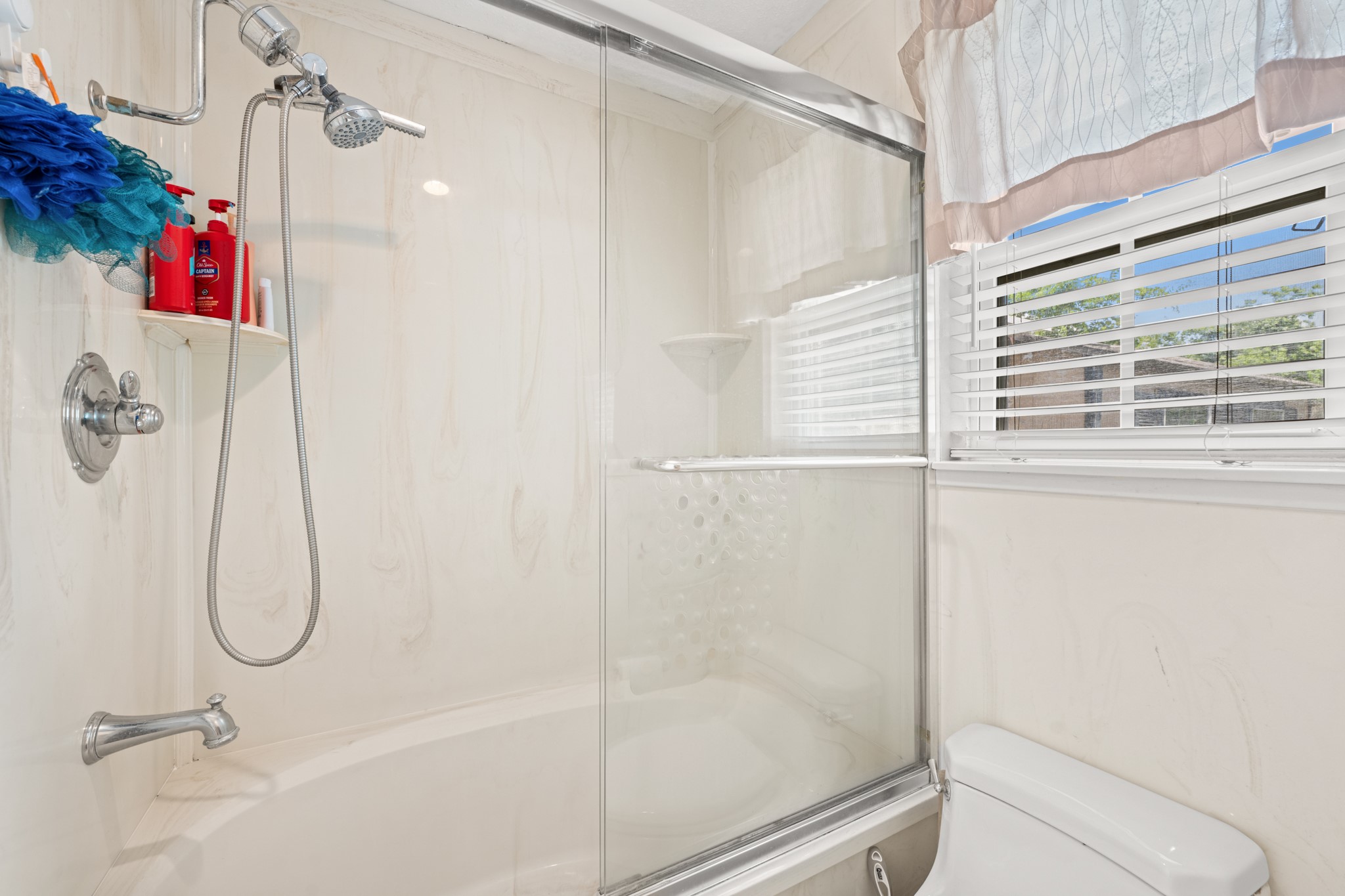 Bright primary bathroom featuring a tub/shower combination with glass enclosure and natural light from the nearby window. Clean finishes and a functional layout create a comfortable and practical everyday space.