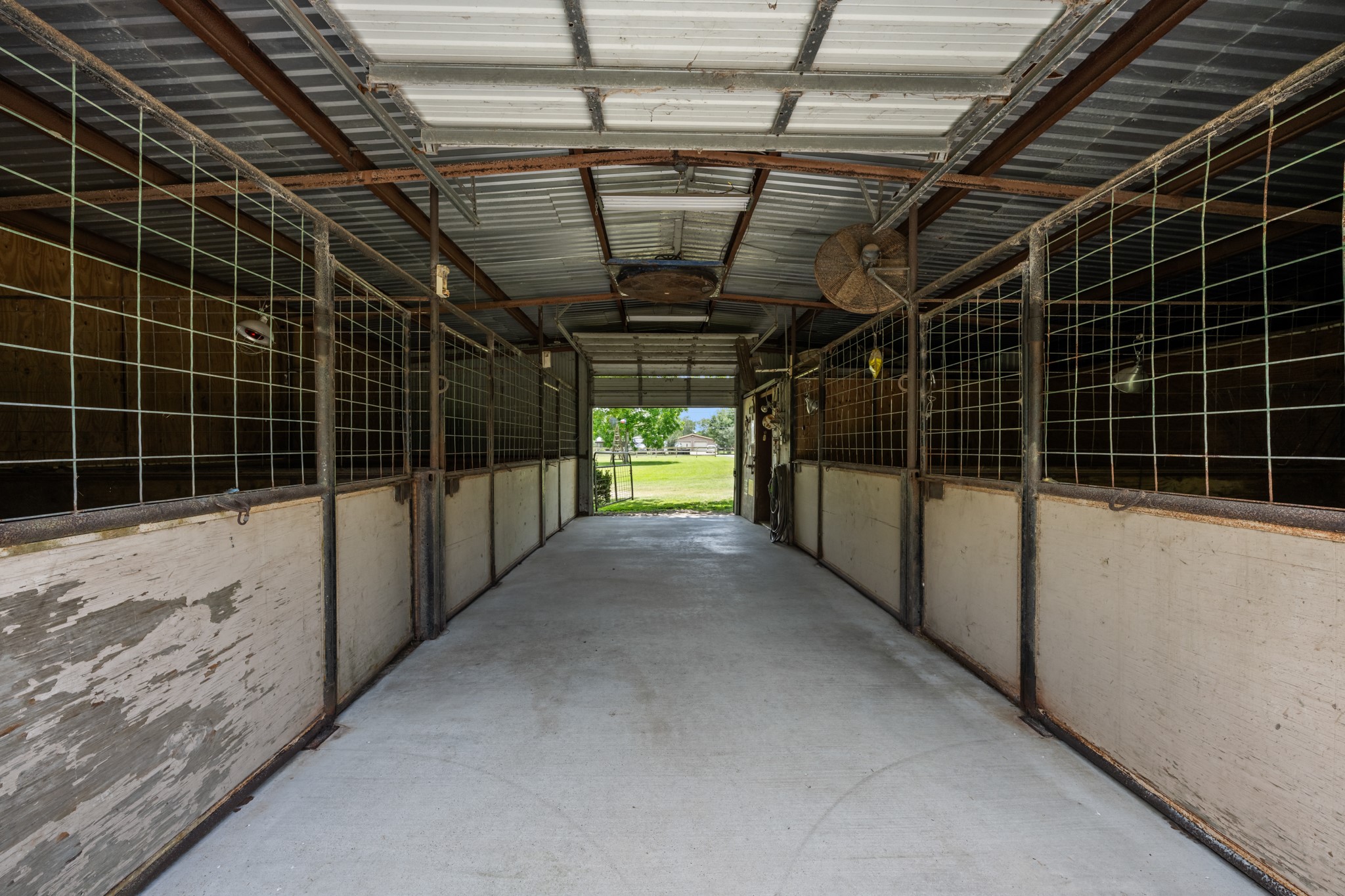 Spacious horse barn featuring multiple enclosed stalls, durable concrete flooring, overhead ventilation, and a wide center aisle for easy access and daily operation. Ideal setup for livestock care and equestrian use.