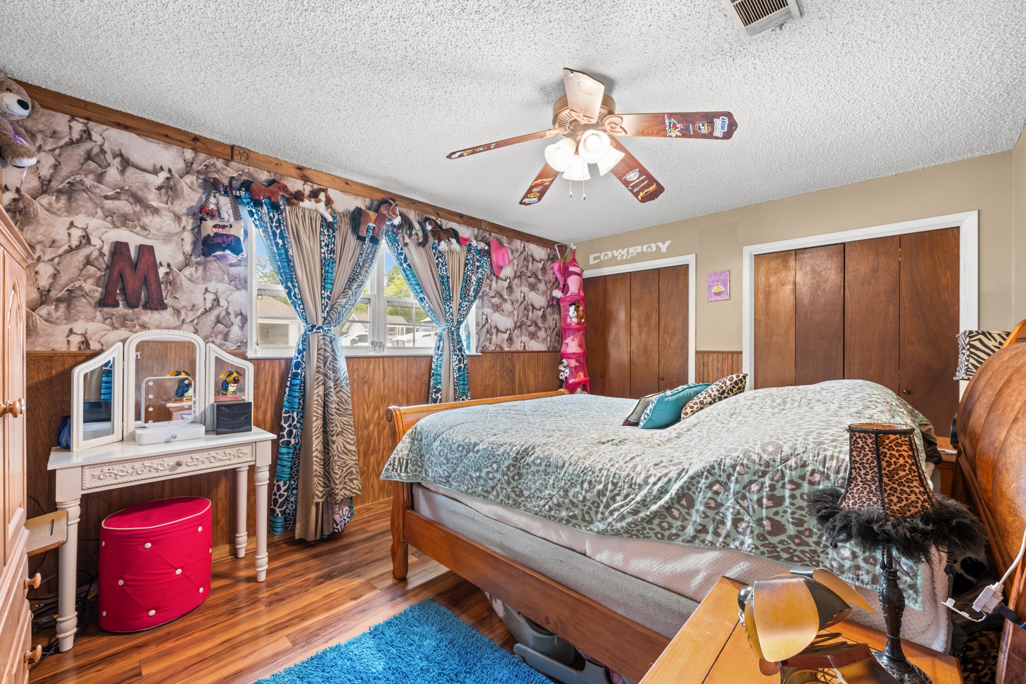 Spacious secondary bedroom featuring wood-look flooring, ample closet storage, and large windows for natural light. Unique design touches and a flexible layout make this space ideal for a bedroom, guest room, or hobby area.