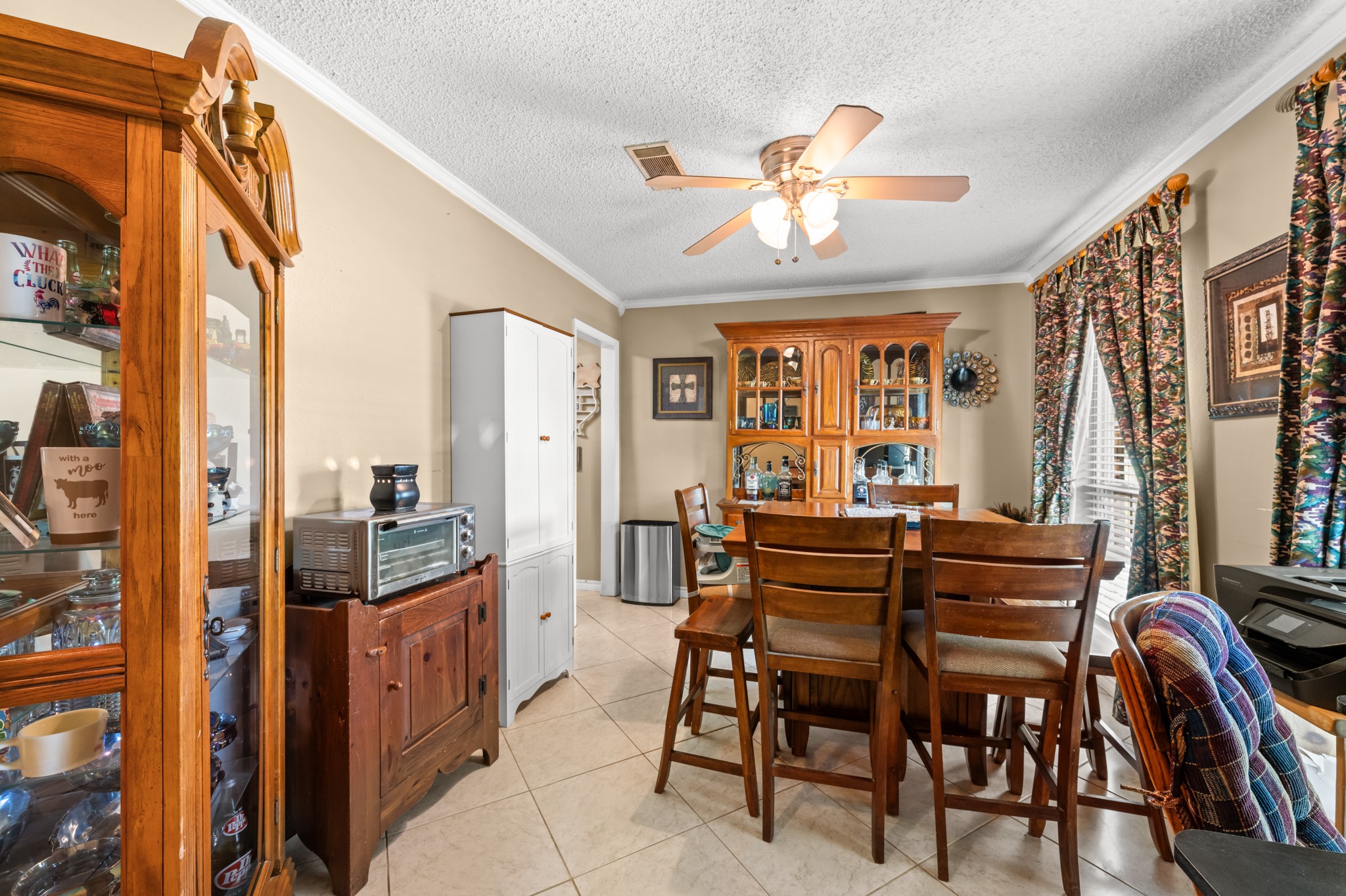 Spacious dining area with tile flooring, crown molding, and large windows that bring in abundant natural light. A functional layout offers plenty of room for everyday meals or hosting family gatherings.