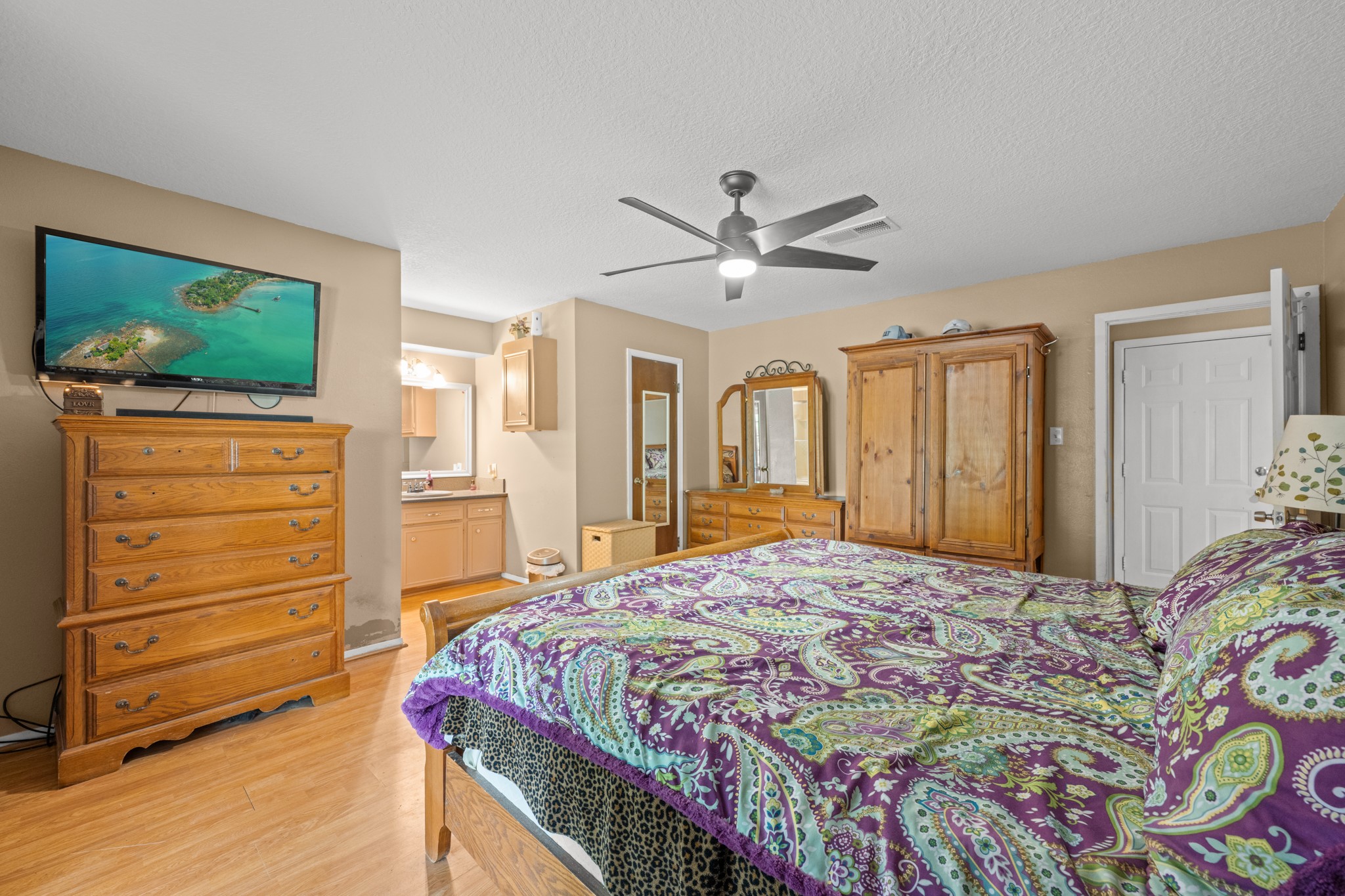Generously sized primary suite featuring wood-look flooring, modern ceiling fan, and a spacious layout with room for additional furnishings. The ensuite vanity area and abundant storage enhance both comfort and everyday functionality.