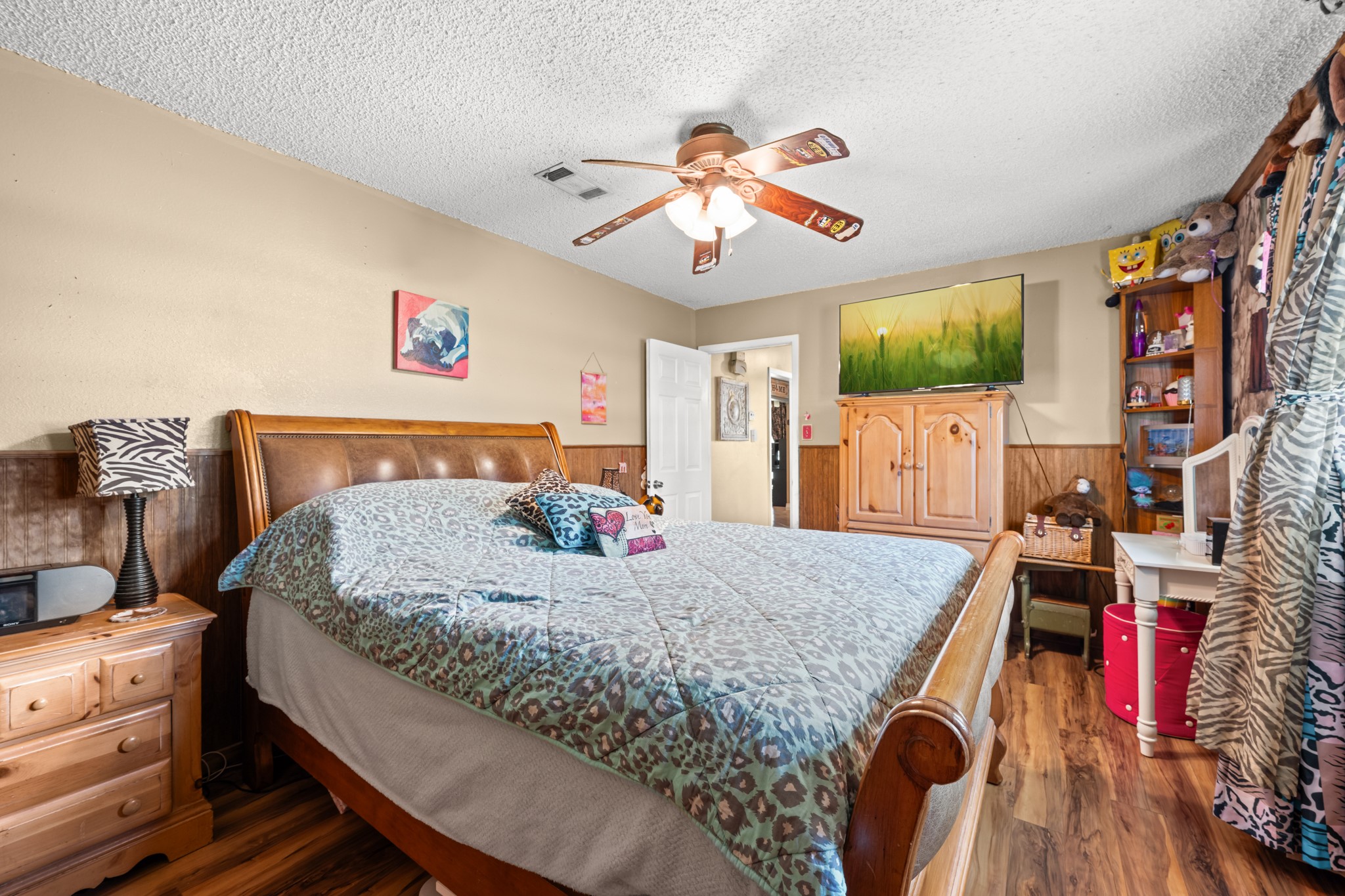 Generously sized secondary bedroom with wood-look flooring, ceiling fan, and ample space for larger furnishings. Large windows and warm finishes create a bright and comfortable retreat with flexible use options.