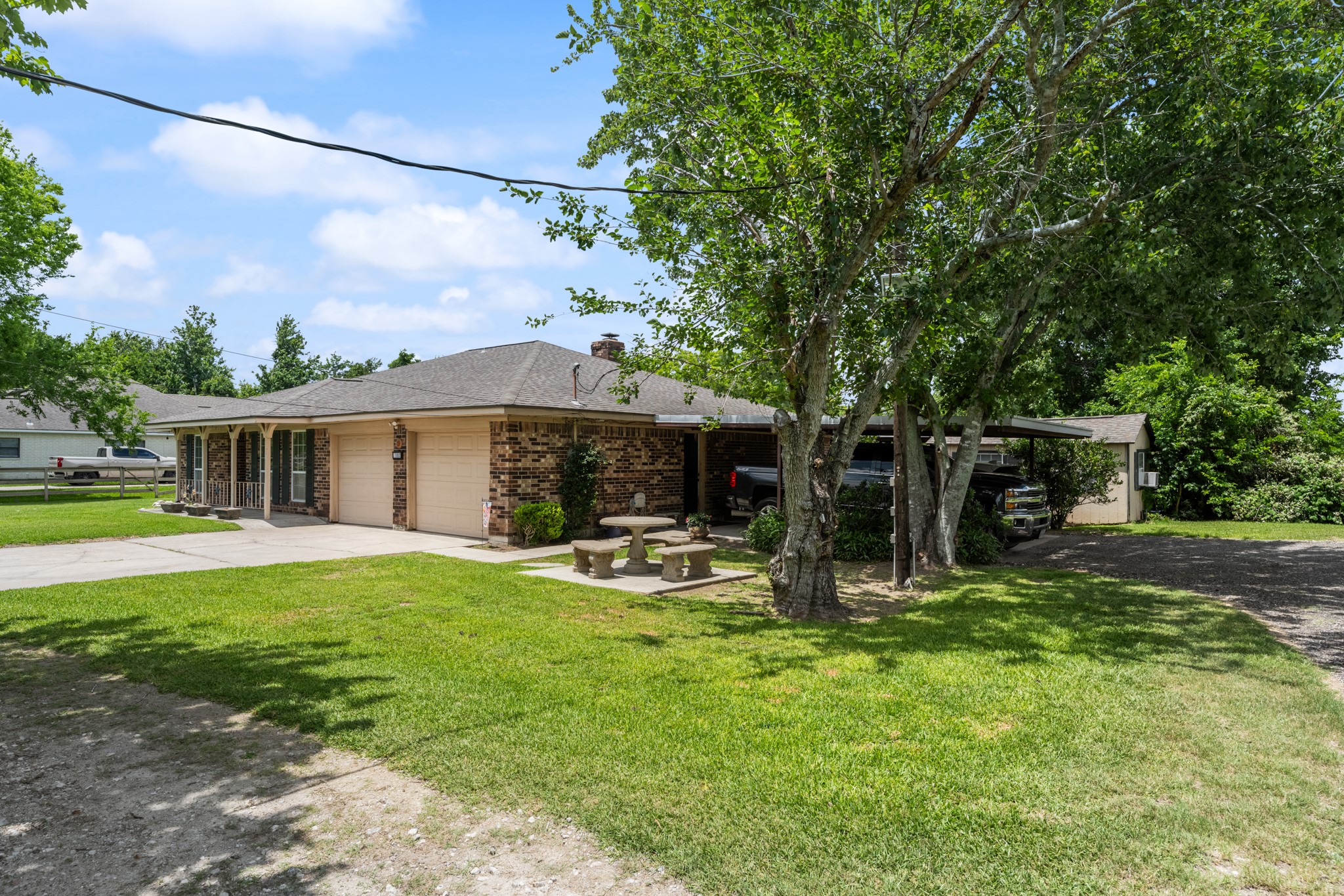 Charming brick exterior with mature shade trees, a spacious driveway, attached garage, and covered parking for added convenience. The expansive front lawn and country-style setting create a welcoming first impression.