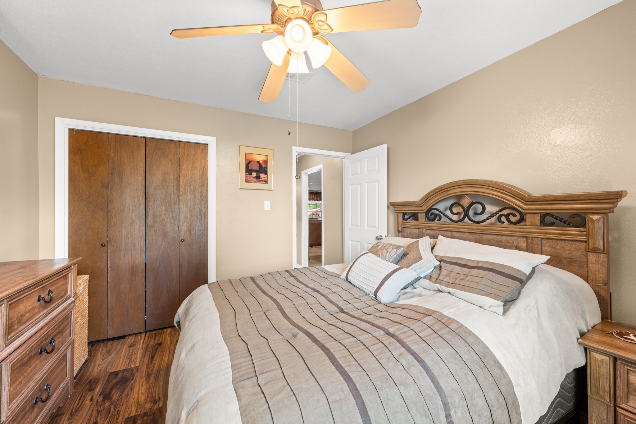 Spacious bedroom with rich wood-look flooring, neutral color palette, and ample closet storage. The ceiling fan and well-designed layout provide a comfortable and relaxing space to unwind.