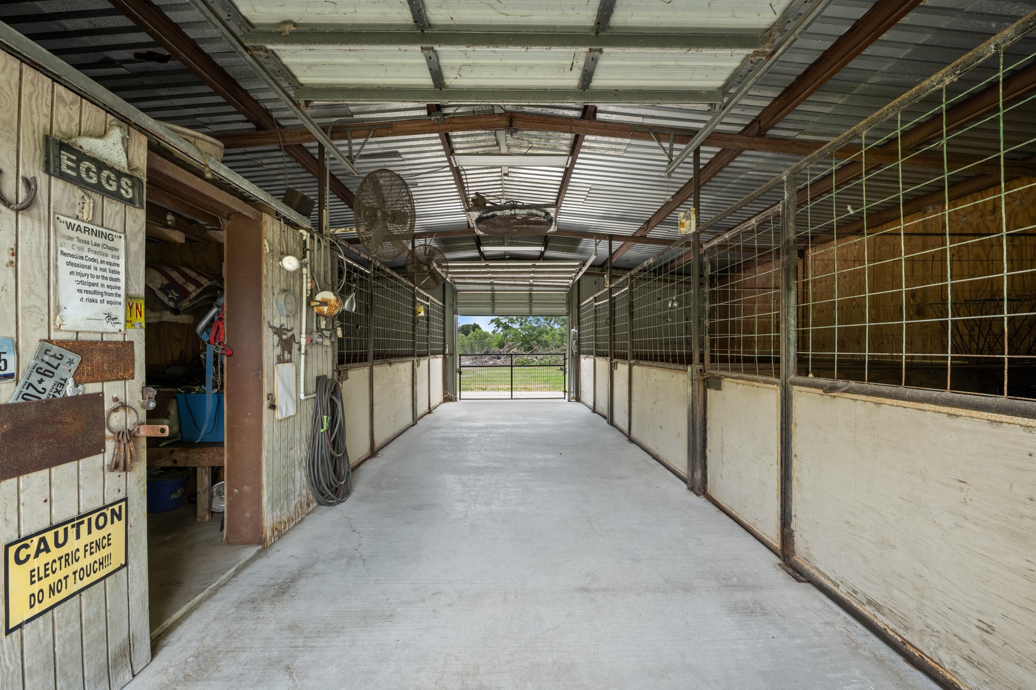 Well-equipped horse barn interior featuring multiple stalls, wide center aisle access, concrete flooring, and dedicated storage space for tack and equipment. Designed for convenient daily care and efficient ranch functionality.