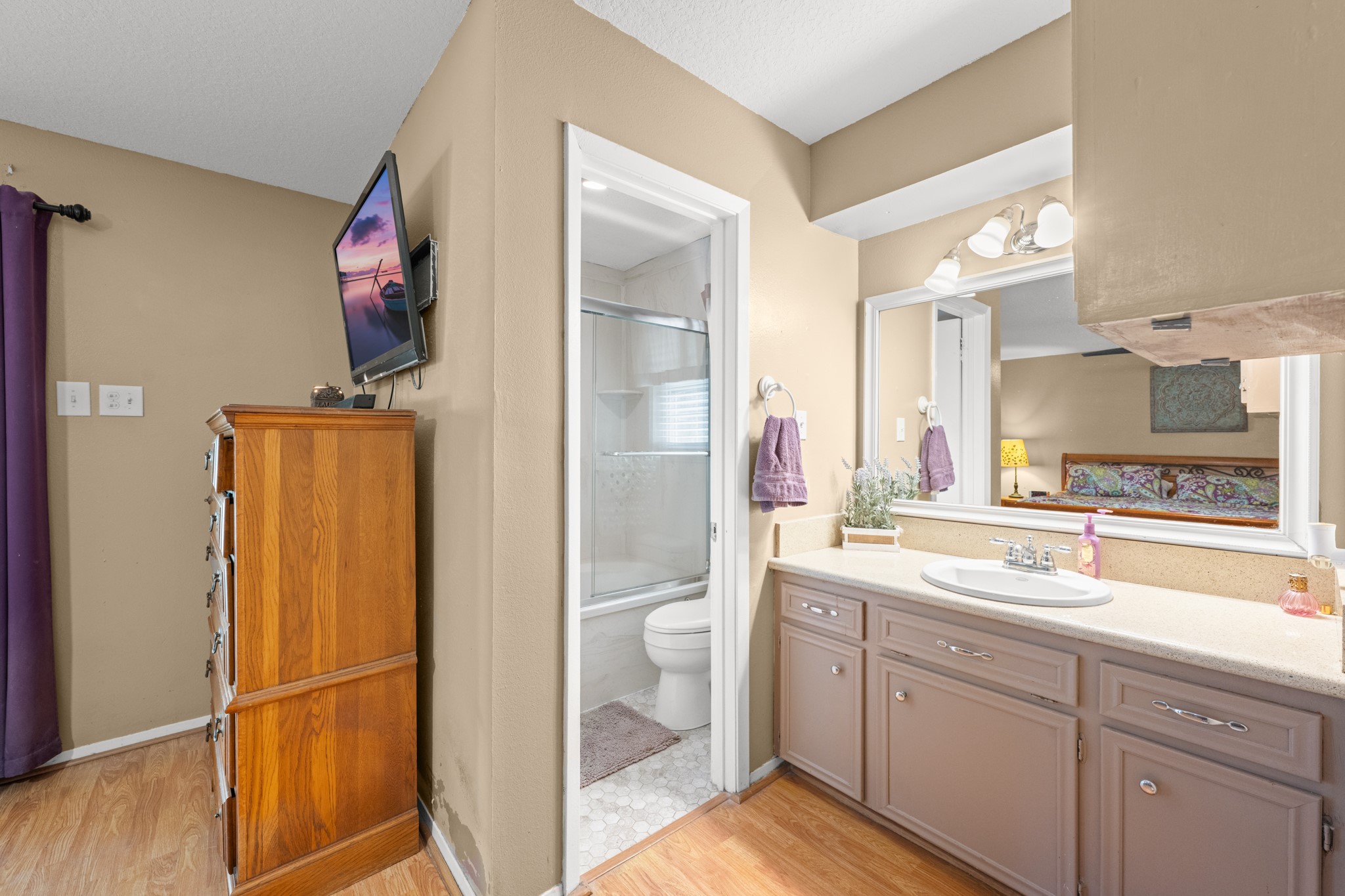 Spacious primary bath vanity area featuring generous counter space, ample cabinetry, and a large mirror with updated lighting. The functional layout offers convenient access to the private bath and shower area for added comfort and privacy.