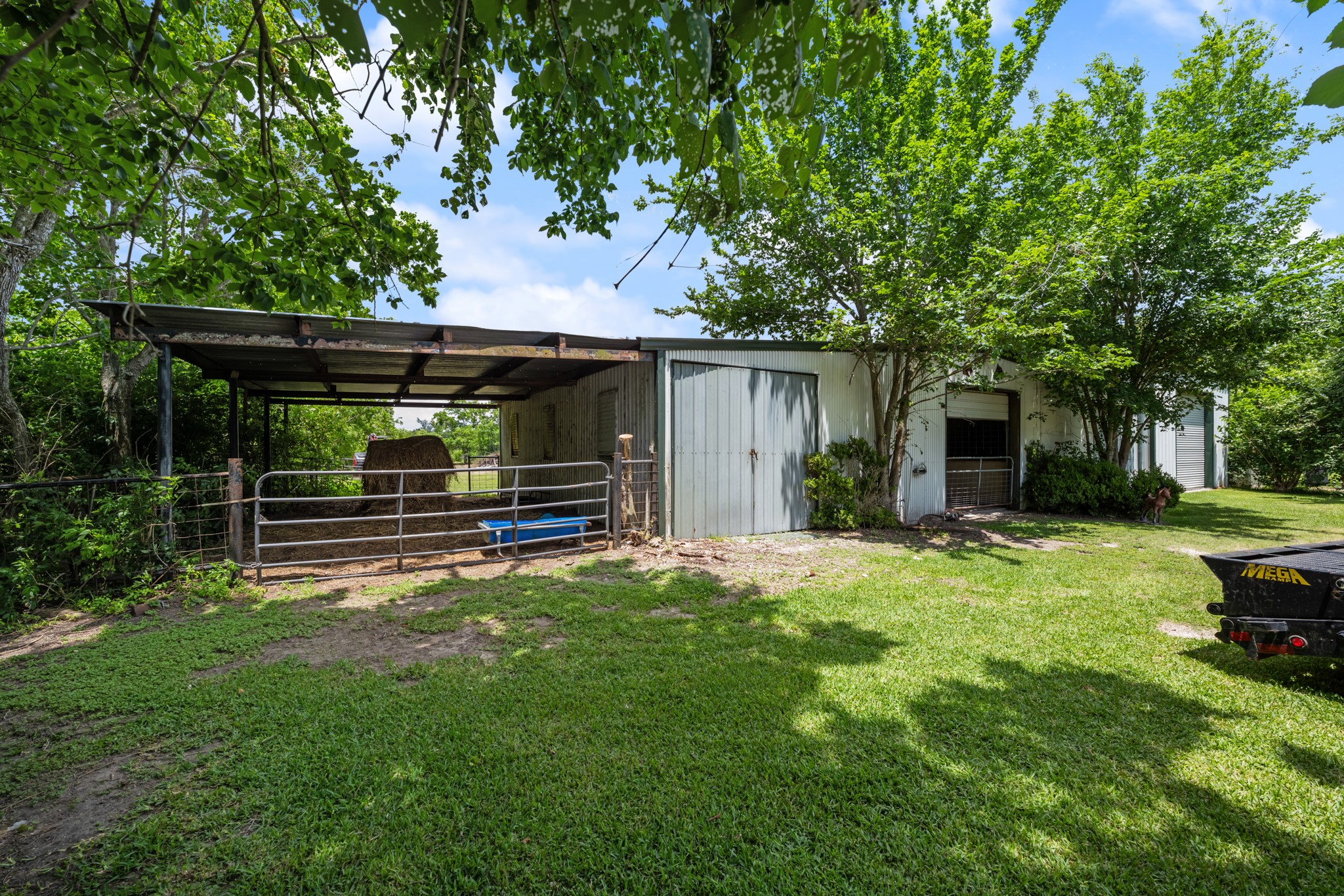 Functional horse barn with covered stalls and fenced areas, offering excellent space for livestock care, feed storage, and everyday  operations. Surrounded by mature trees and open green space for a peaceful country setting.