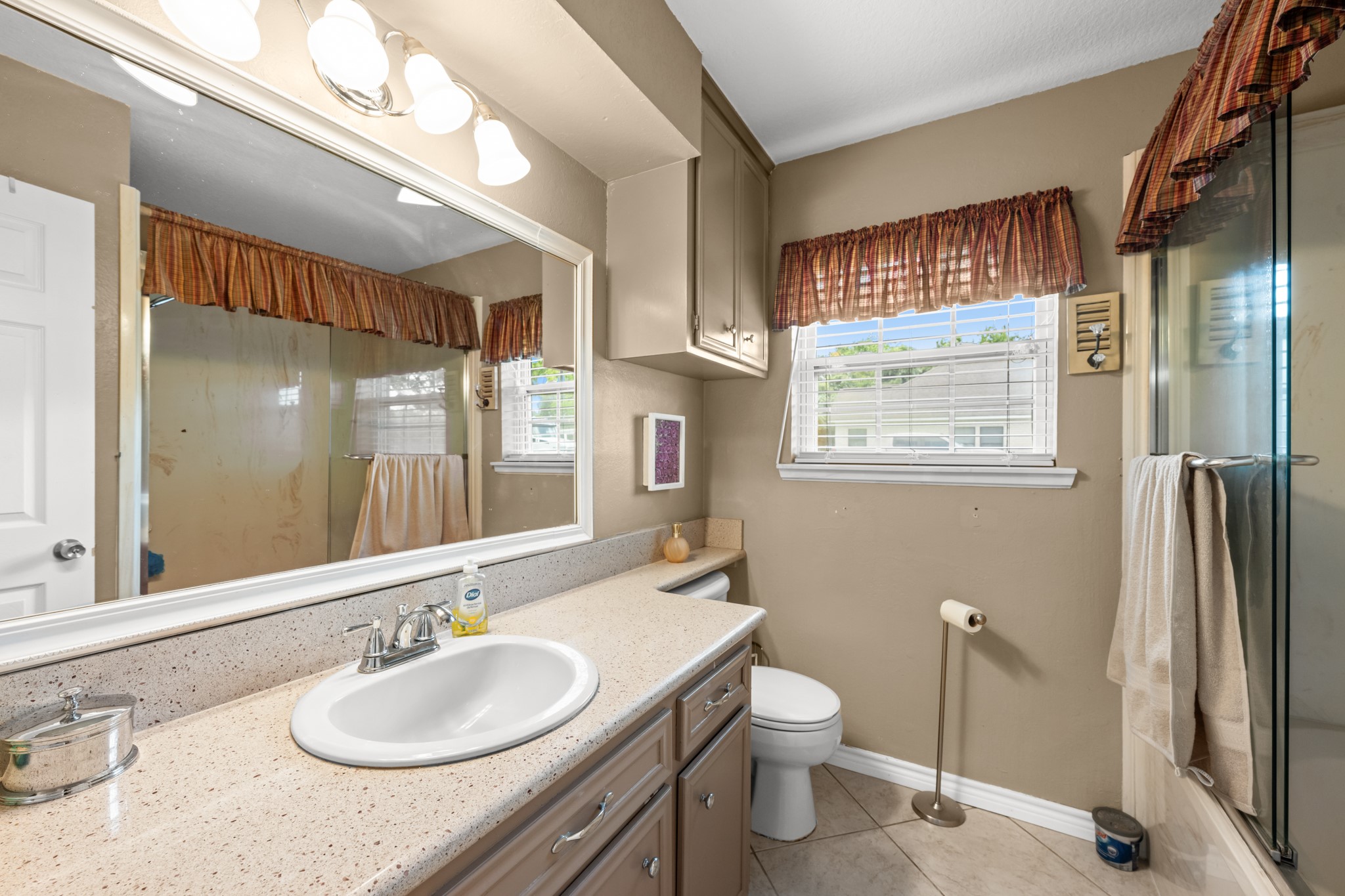 Well-appointed secondary bathroom featuring an oversized vanity with generous counter space, ample cabinetry, and a large mirror. Natural light and a glass-enclosed shower create a bright and functional everyday space.