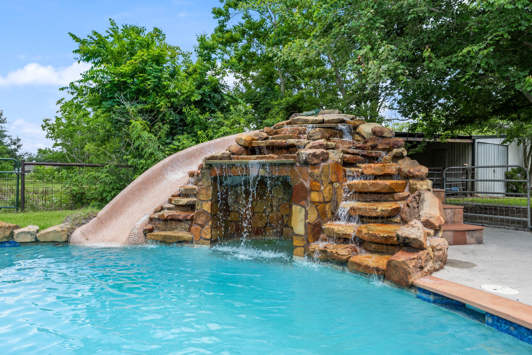 Resort-style pool feature with a custom rock waterfall, cascading water elements, and an impressive built-in slide that creates a true private retreat. Perfect for outdoor entertaining and summer fun.