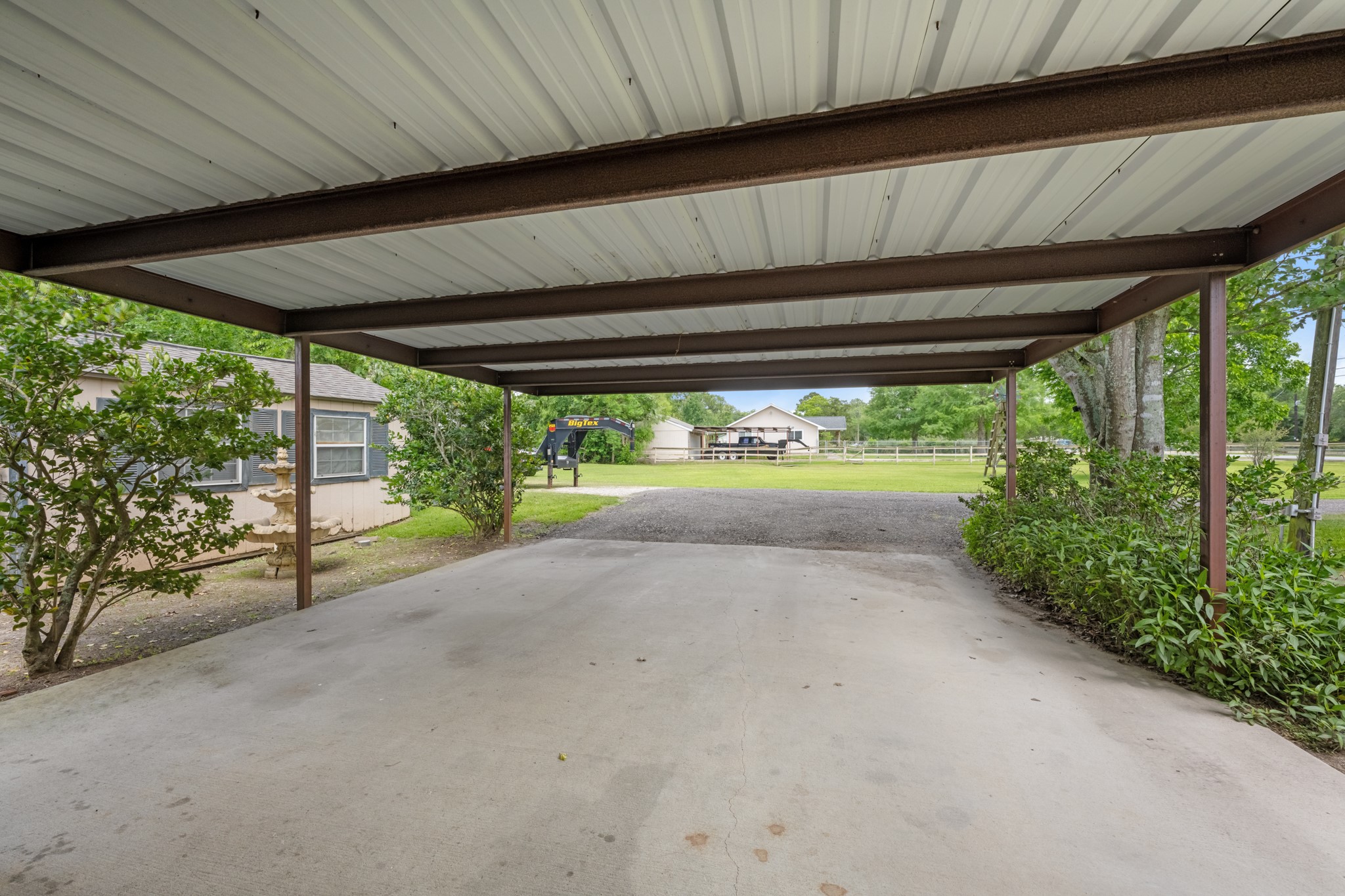 Covered parking area with ample space for two vehicles, trailers, or recreational equipment. The surrounding open yard and mature landscaping add to the propertys versatility and country-style appeal.