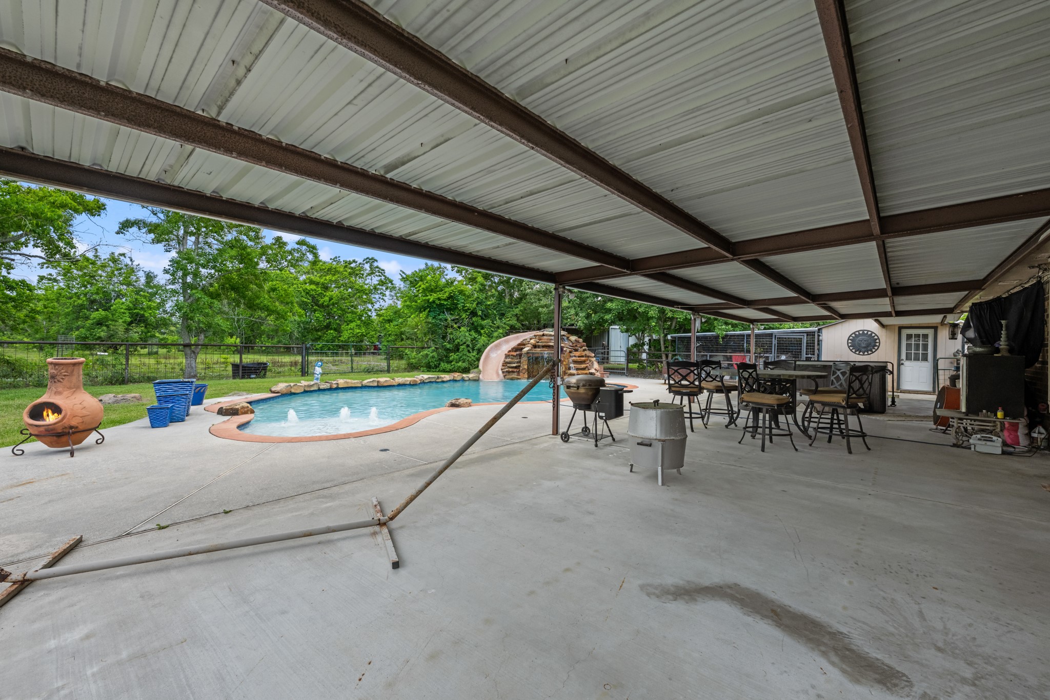 Resort-style backyard featuring a sparkling pool with rock waterfall slide, expansive covered patio, and multiple seating areas designed for outdoor entertaining. The spacious setup offers the perfect blend of relaxation, recreation, and year-round enjoyment.
