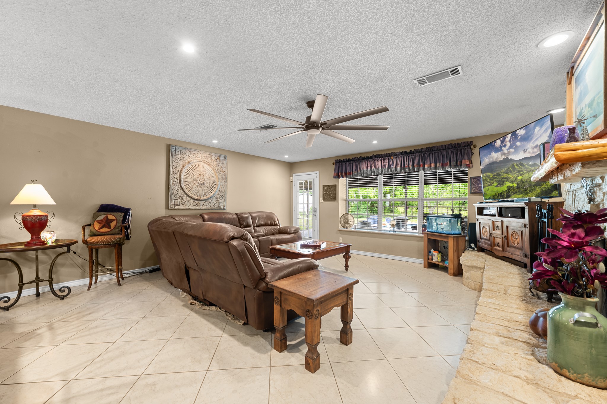 Spacious open living room featuring a beautiful stone fireplace, recessed lighting, and oversized windows overlooking the property. The expansive layout and neutral finishes provide the perfect setting for everyday living and entertaining alike.