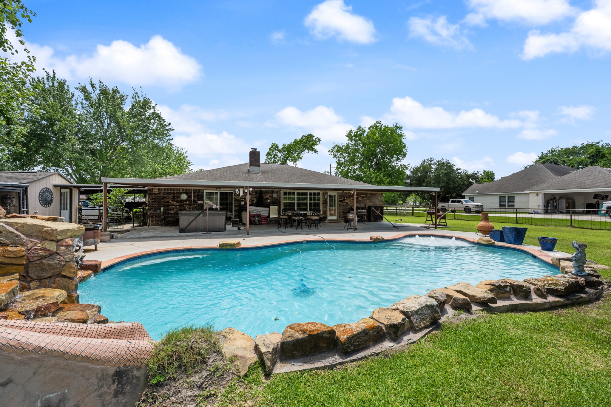 Spacious backyard oasis featuring a resort-style pool with a custom rock waterfall slide, expansive green space, and a large covered patio perfect for outdoor entertaining and relaxing year-round.