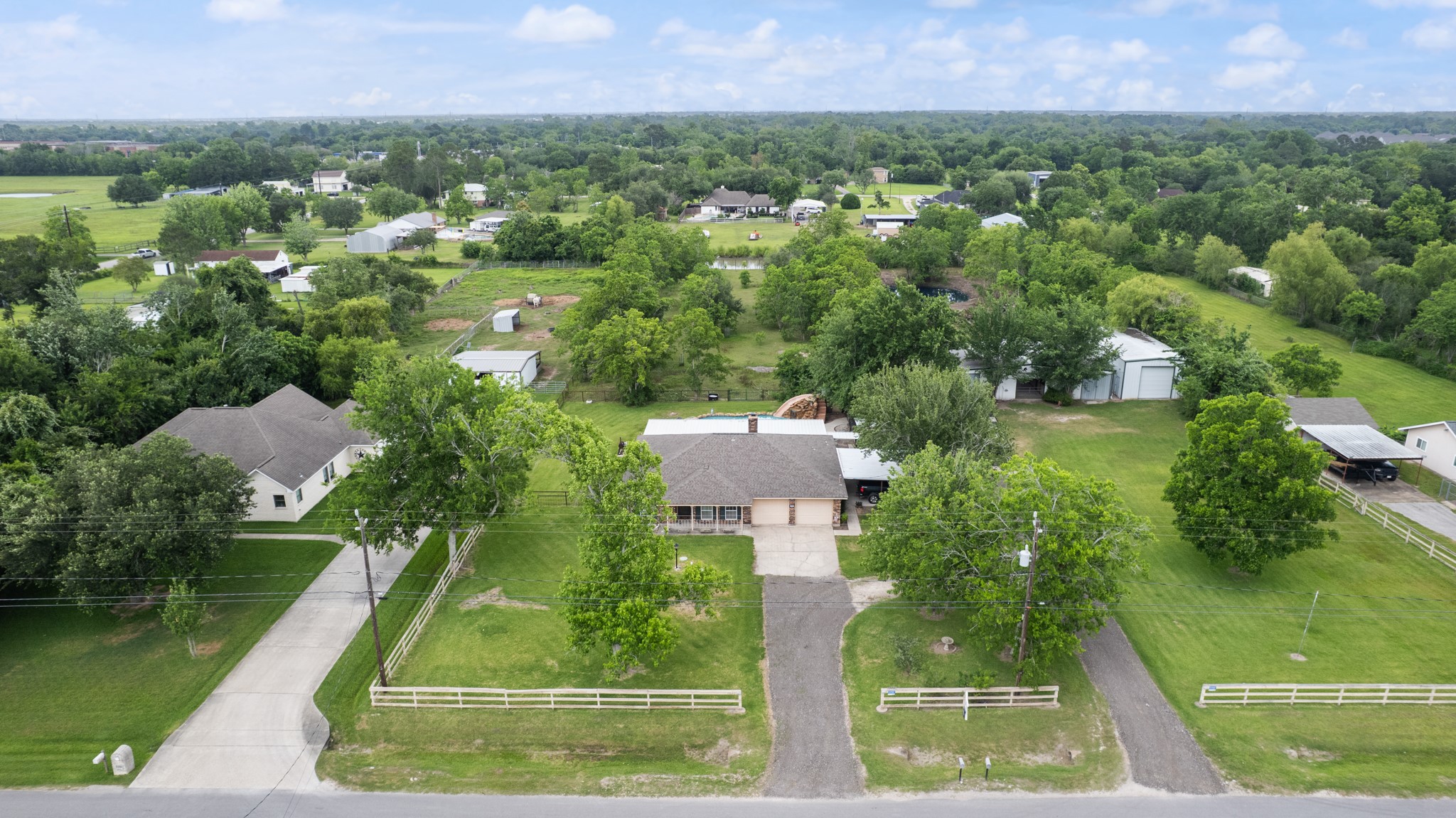 Expansive aerial view showcasing the home, pool area, horse barn, insulated workshop, and sprawling acreage surrounded by mature trees. This unique property offers a blend of residential comfort, outdoor recreation, and functional space for hobbies or livestock.