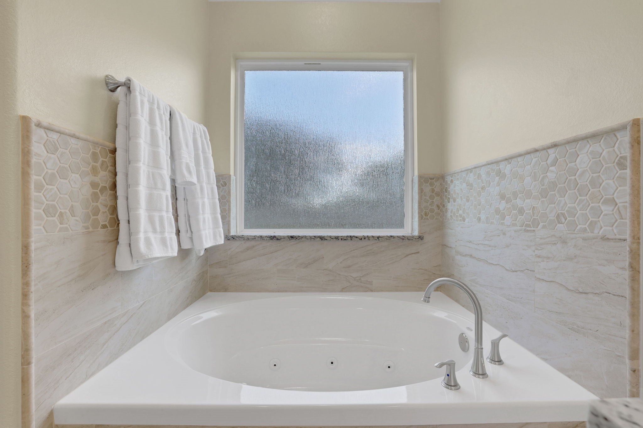 Luxurious bathroom featuring a spacious jetted tub, elegant tile accents, and a frosted window for privacy.