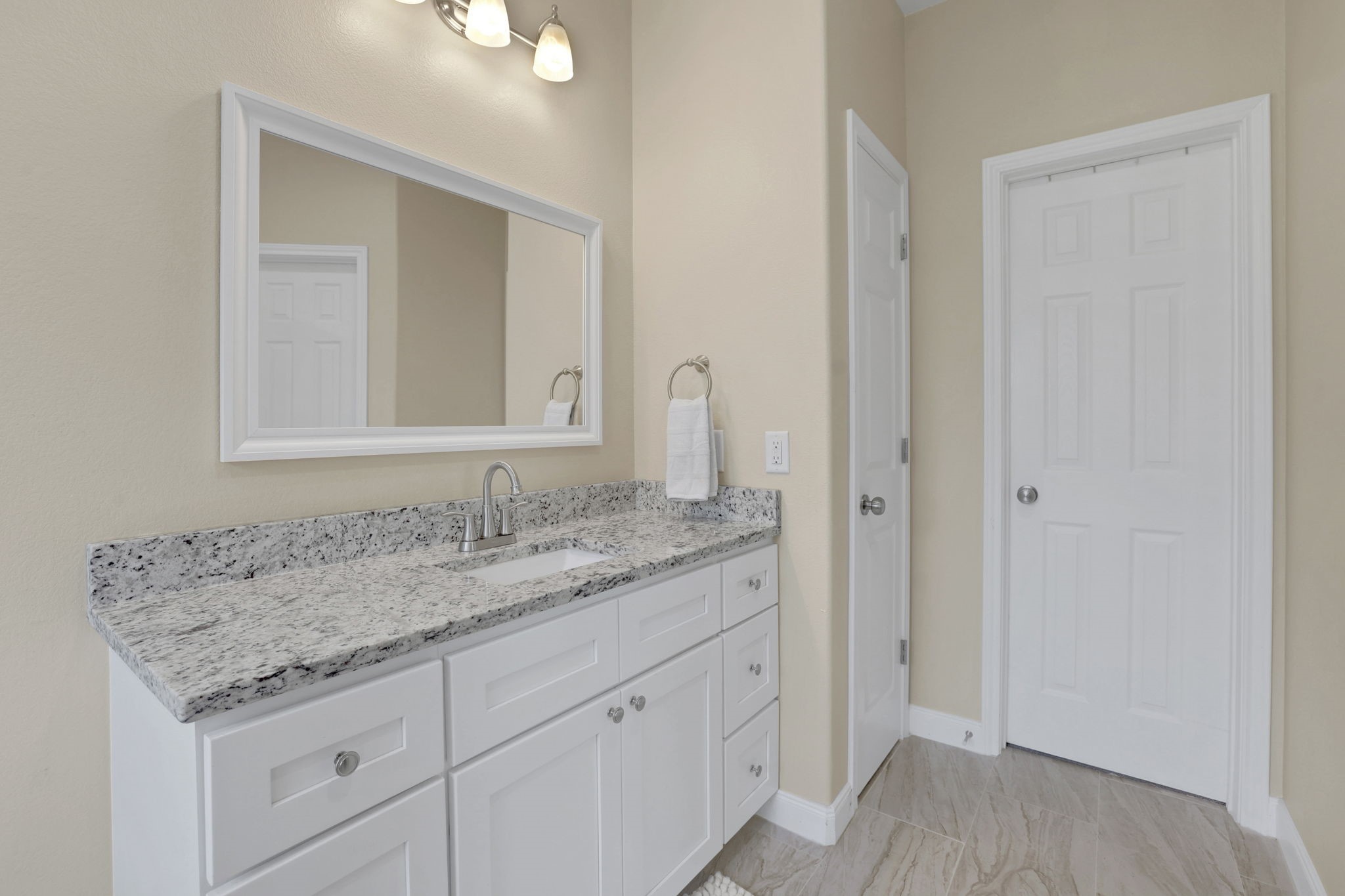 Elegant primary bathroom featuring a sleek granite countertop, modern white vanity, and ample storage, complemented by soft lighting and neutral walls.