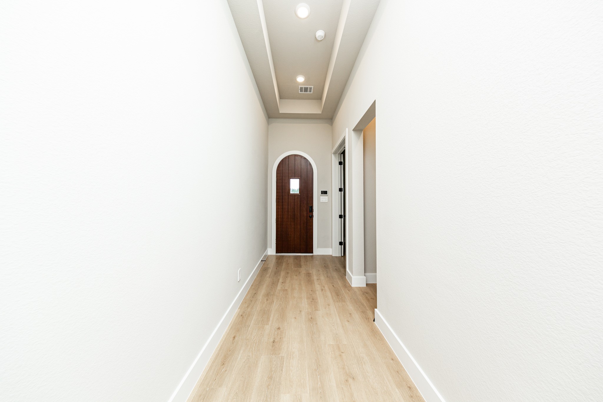 This long entryway features wood-look flooring and a tray ceiling. This Spanish-style front door serves as a bold architectural focal point, featuring a classic round arch top and a rich, dark-stained wood finish that provides a deep contrast against the home's light-colored walls