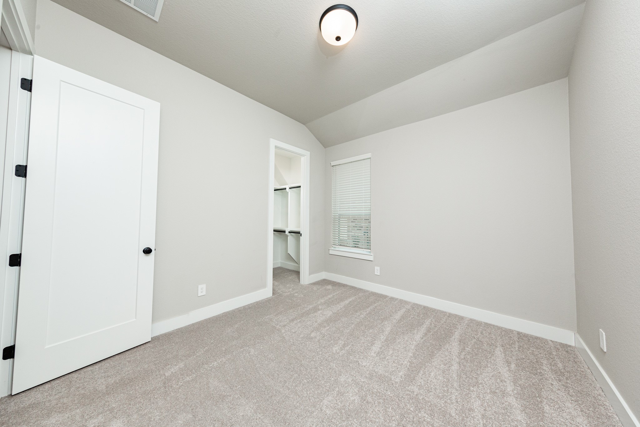 This secondary bedroom features a sloped ceiling, plush carpet flooring, a large window, a walk-in closet, and an ensuite secondary bathroom.