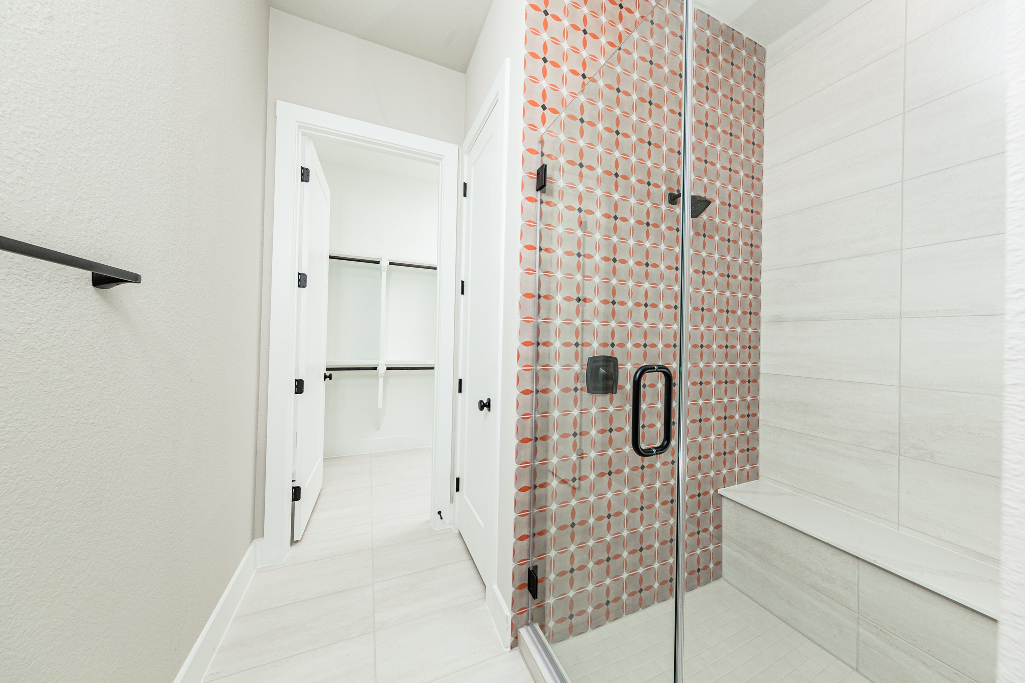 The walk-in shower includes a convenient, integrated white bench, offering comfort and a high-end, custom appearance. This modern shower features a striking two-tile design that balances bold patterns with clean, neutral surfaces.