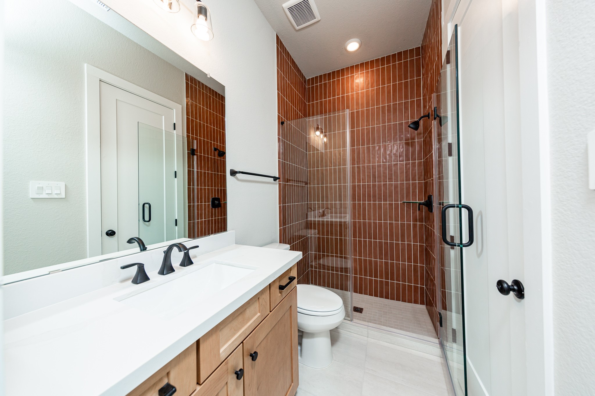 This ensuite secondary bathroom features a modern vanity, large walk-in shower with gorgeous modern tile surround, and modern black matte finishes.