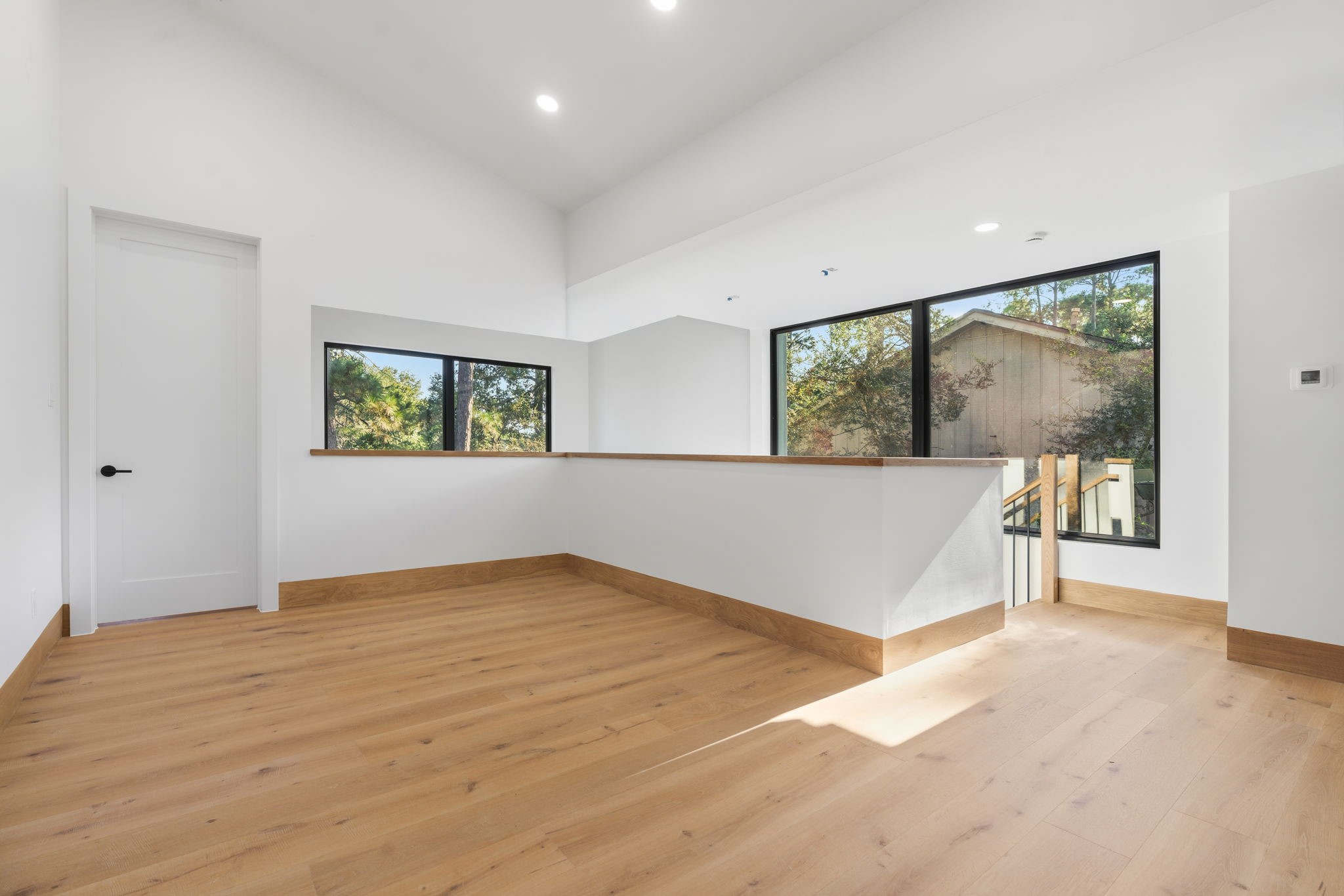 Spacious second-floor game room / sitting area featuring high ceilings, warm wood flooring, and large windows that fill the space with natural light